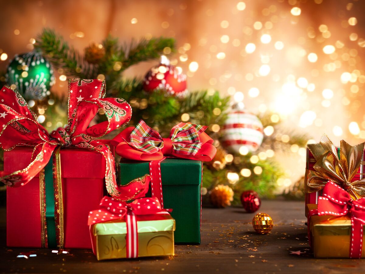 Festlich verpackte Weihnachtsgeschenke mit roten und grünen Schleifen vor einem geschmückten Weihnachtsbaum mit Lichterglanz. Bokeh.