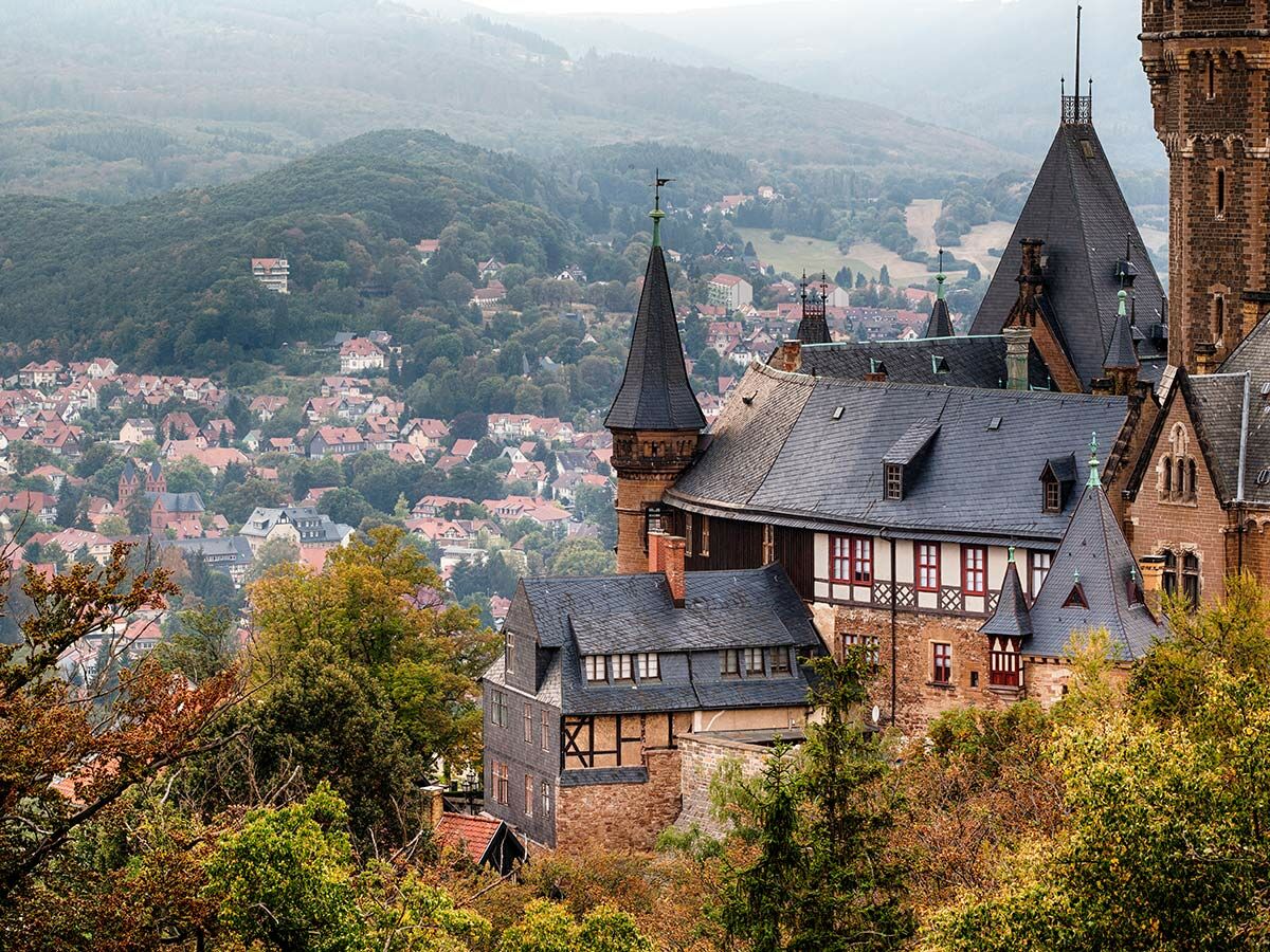 Historisches Schloss Wernigerode im Harz im Herbst, hoch über einer malerischen Stadt mit roten Dächern und bewaldeten Hügeln.