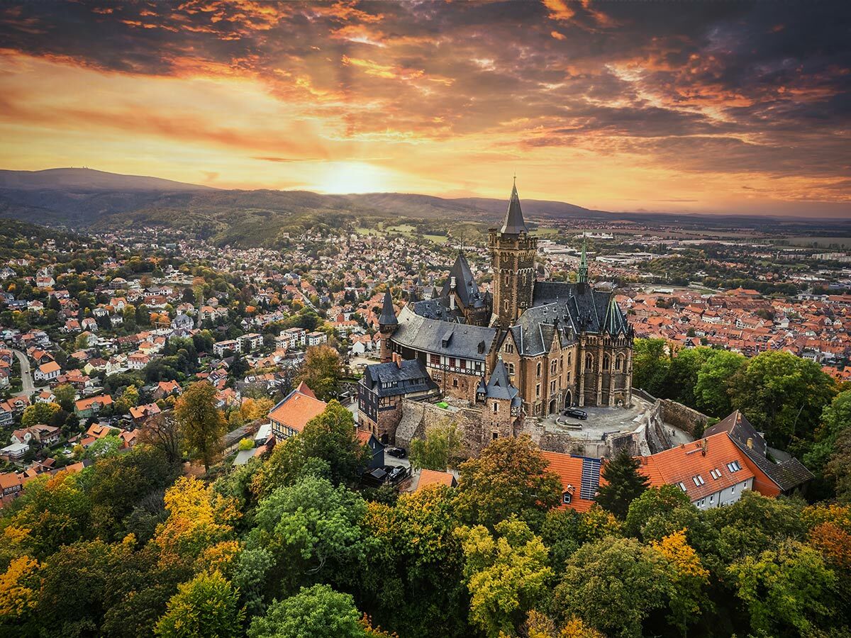 Wernigerode Schloss bei Sonnenuntergang über Stadt mit roten Dächern und herbstlichen Bäumen im Harz.
