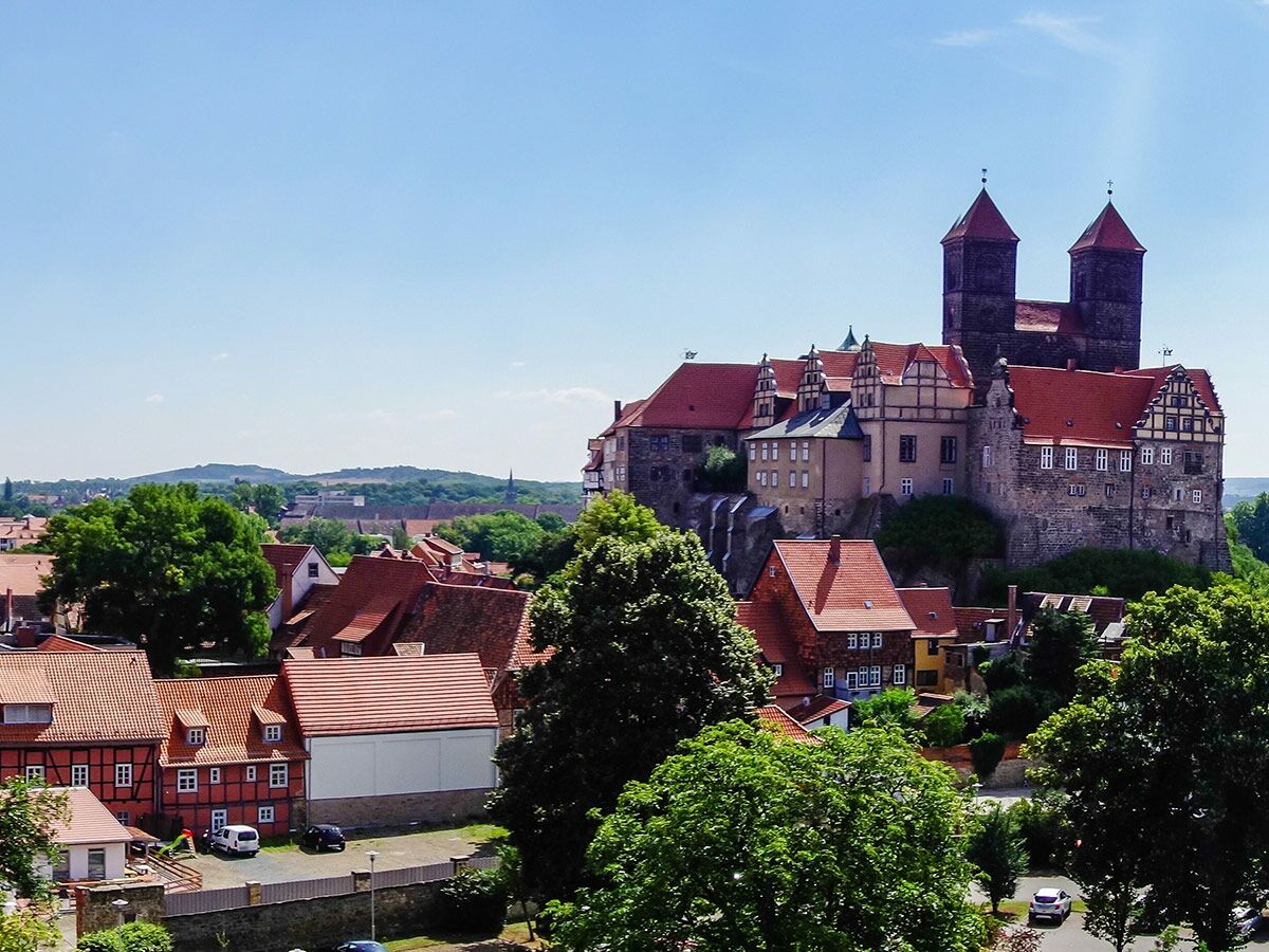 Blick auf den historischen Schlossberg Quedlinburg mit der Stiftskirche St. Servatii, umgeben von roten Dächern und Fachwerkhäusern unter blauem Himmel.