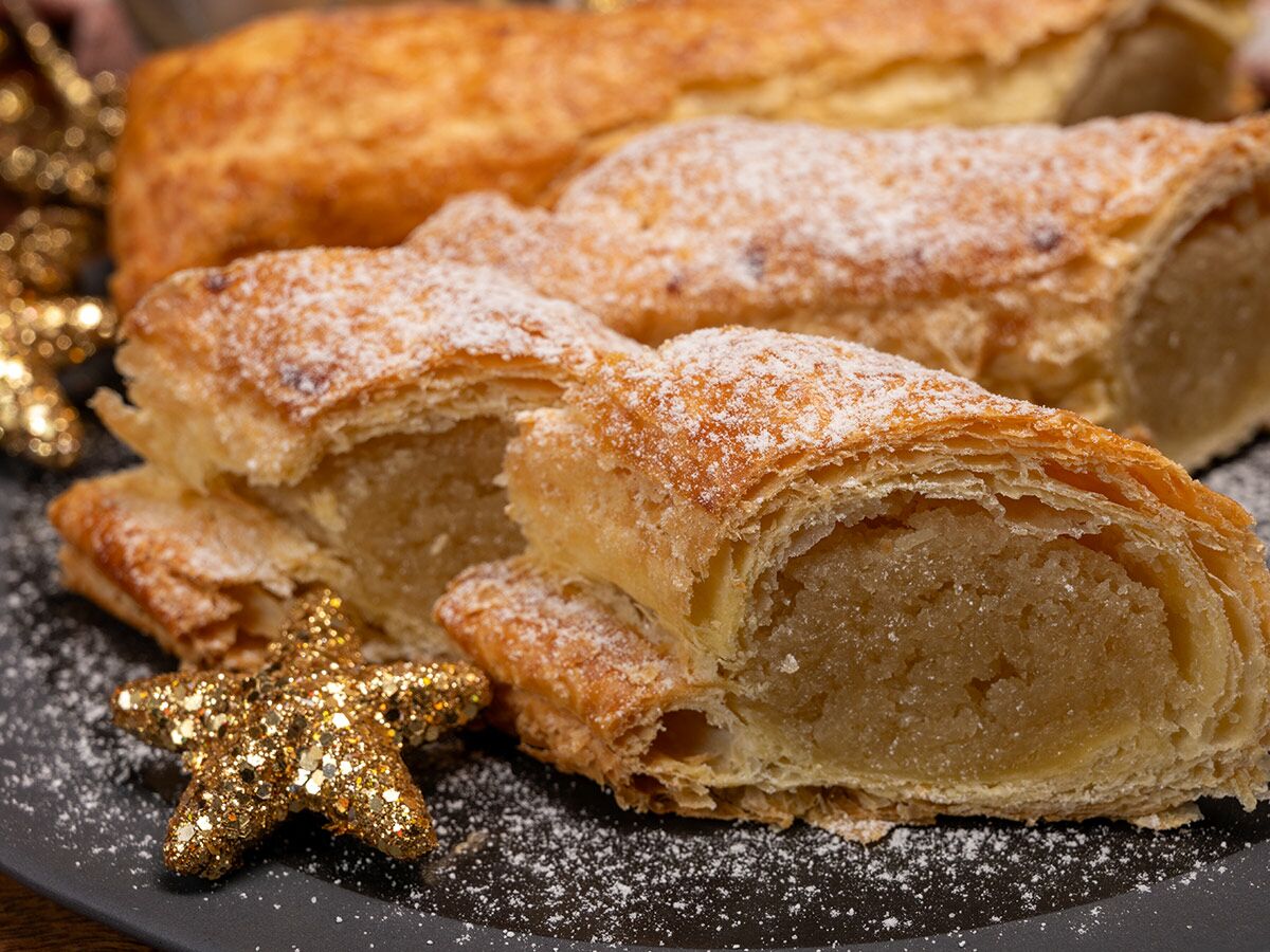 Nahaufnahme von goldbraunen Marzipan Gebäckstücken mit Puderzucker und goldener Weihnachtsstern-Dekoration auf dunklem Teller.