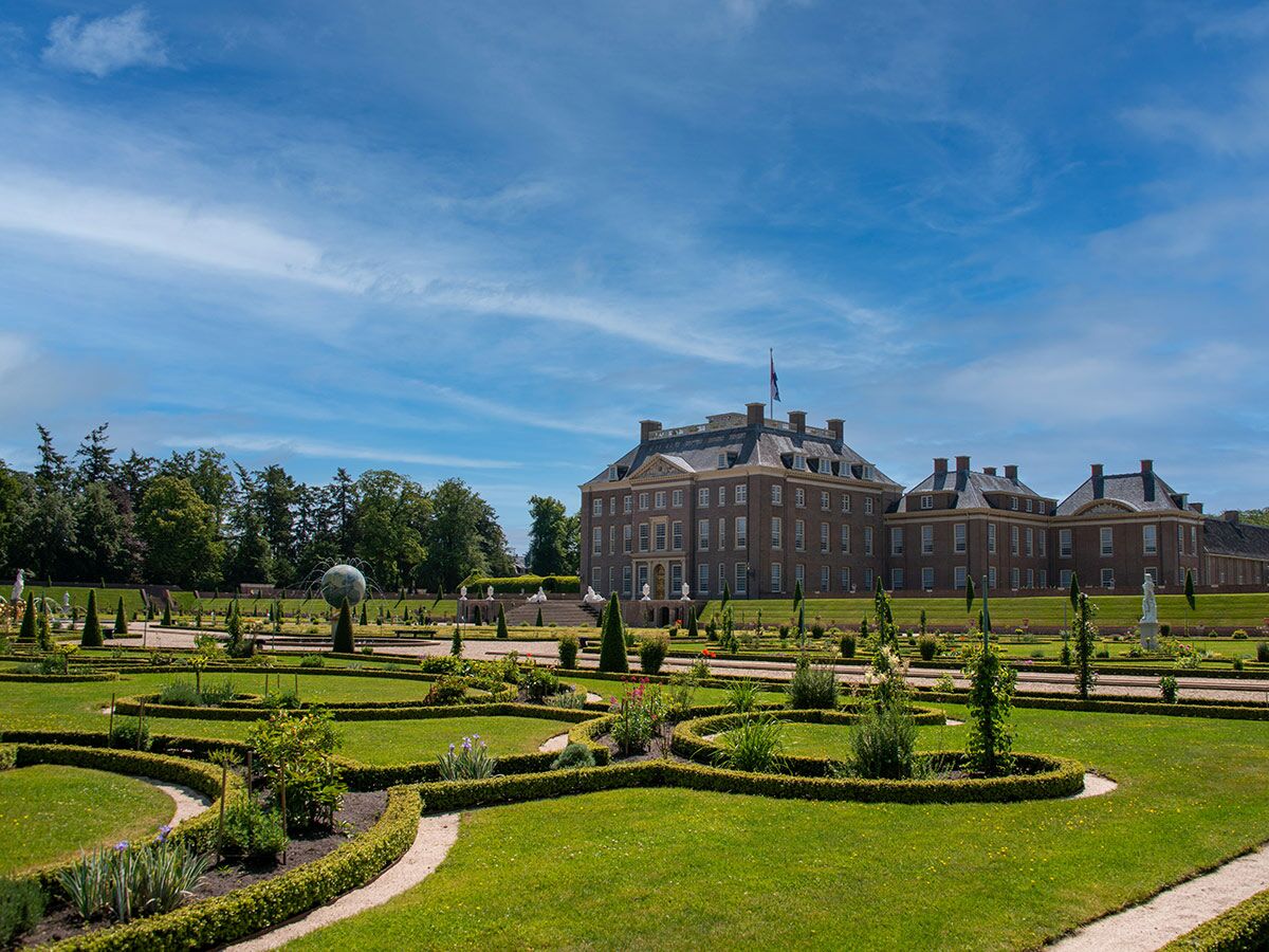 Blick auf ein prächtiges historisches Schloss mit einem weitläufigen, gepflegten Barockgarten und blauem Himmel an einem sonnigen Tag.