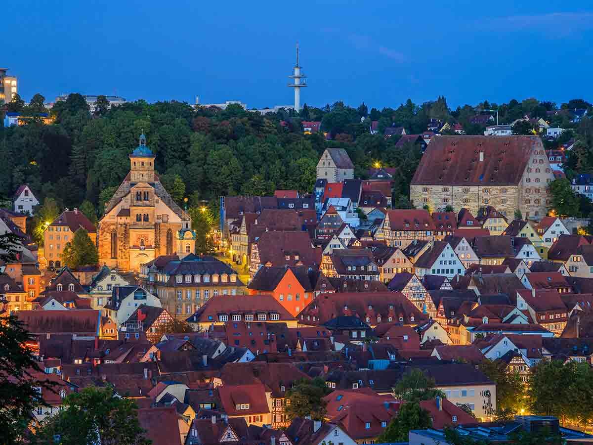 Panoramablick auf Tübingens historische Altstadt zur blauen Stunde, mit beleuchteter Stiftskirche und traditionellen roten Dächern.
