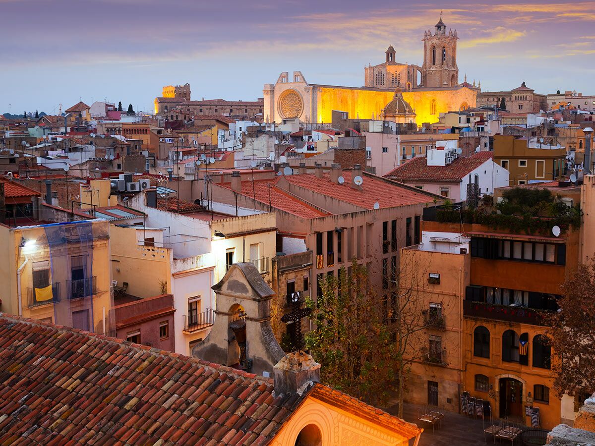 Panoramablick auf die beleuchtete Kathedrale von Tarragona bei Dämmerung über den roten Dächern der Altstadt.