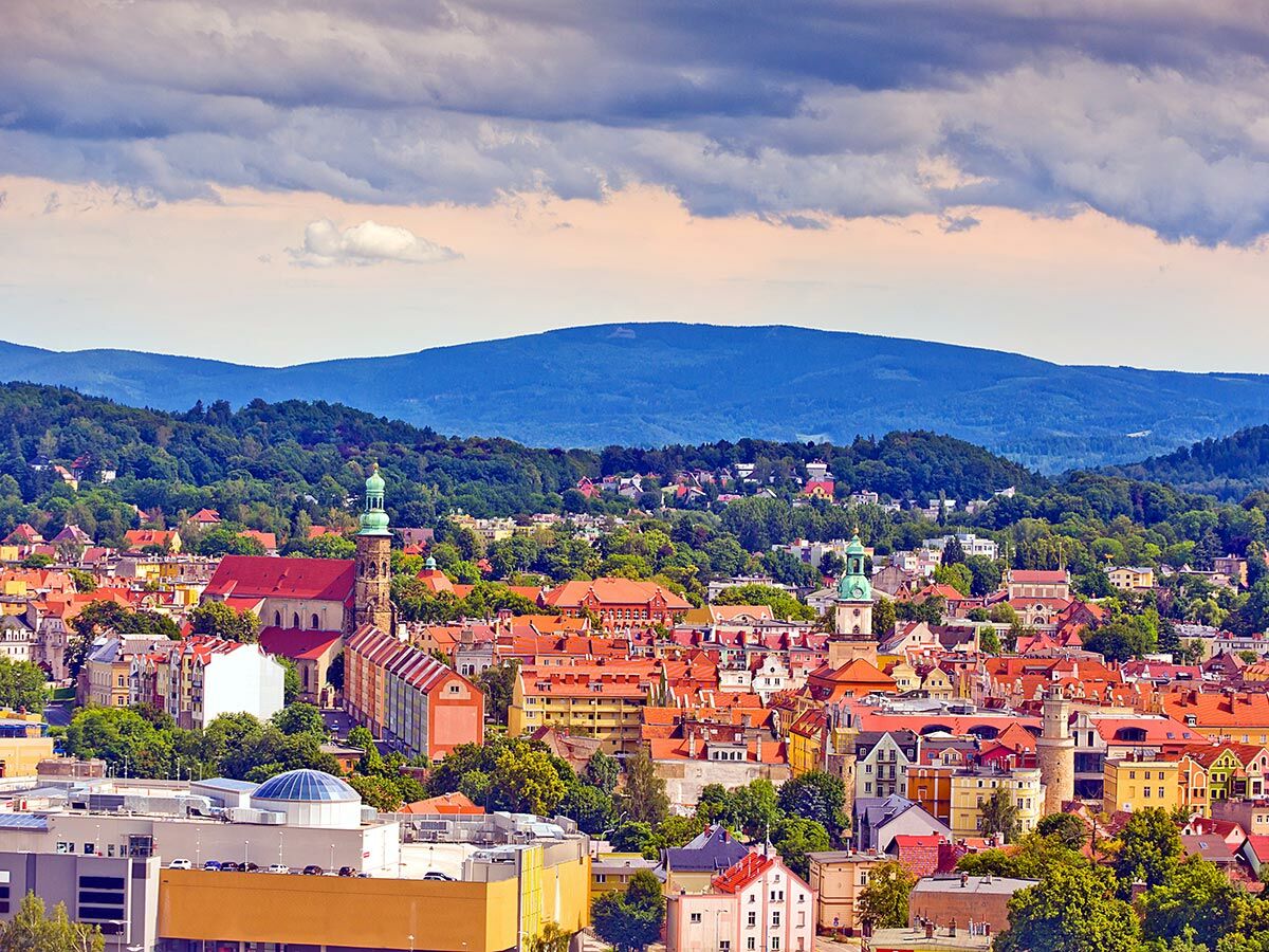 Weitläufiges Panorama der Stadt Wałbrzych, Polen, mit roten Dächern, grünen Sudetenbergen und Kirchen.