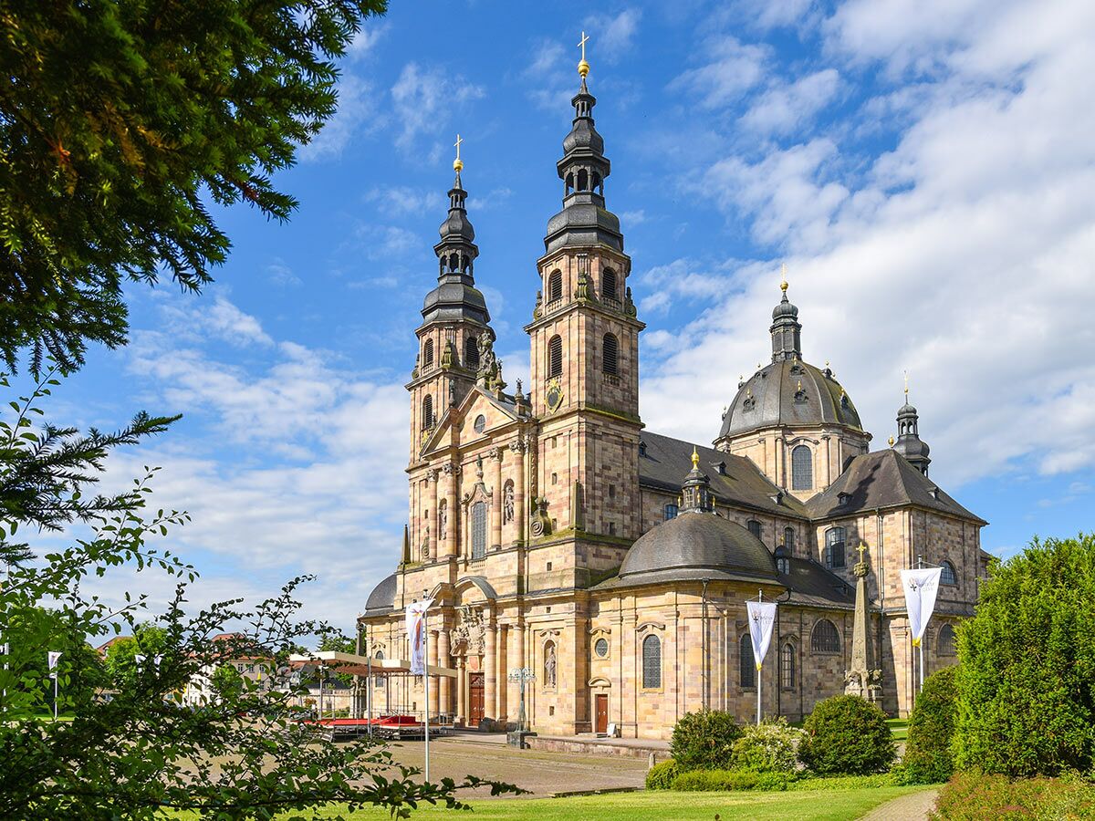 Ansicht des Fuldaer Doms, einer prächtigen Barock-Kathedrale mit Türmen, Kuppeln und Fassadendetails unter blauem Himmel.