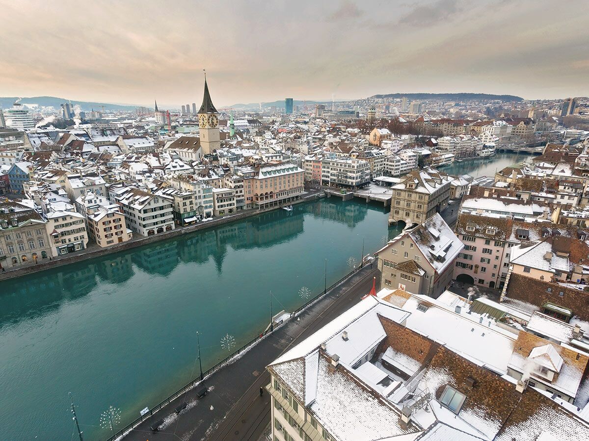 Luftaufnahme von Zürich im Winter mit schneebedeckten Dächern, dem Fluss Limmat und der Grossmünsterkirche.
