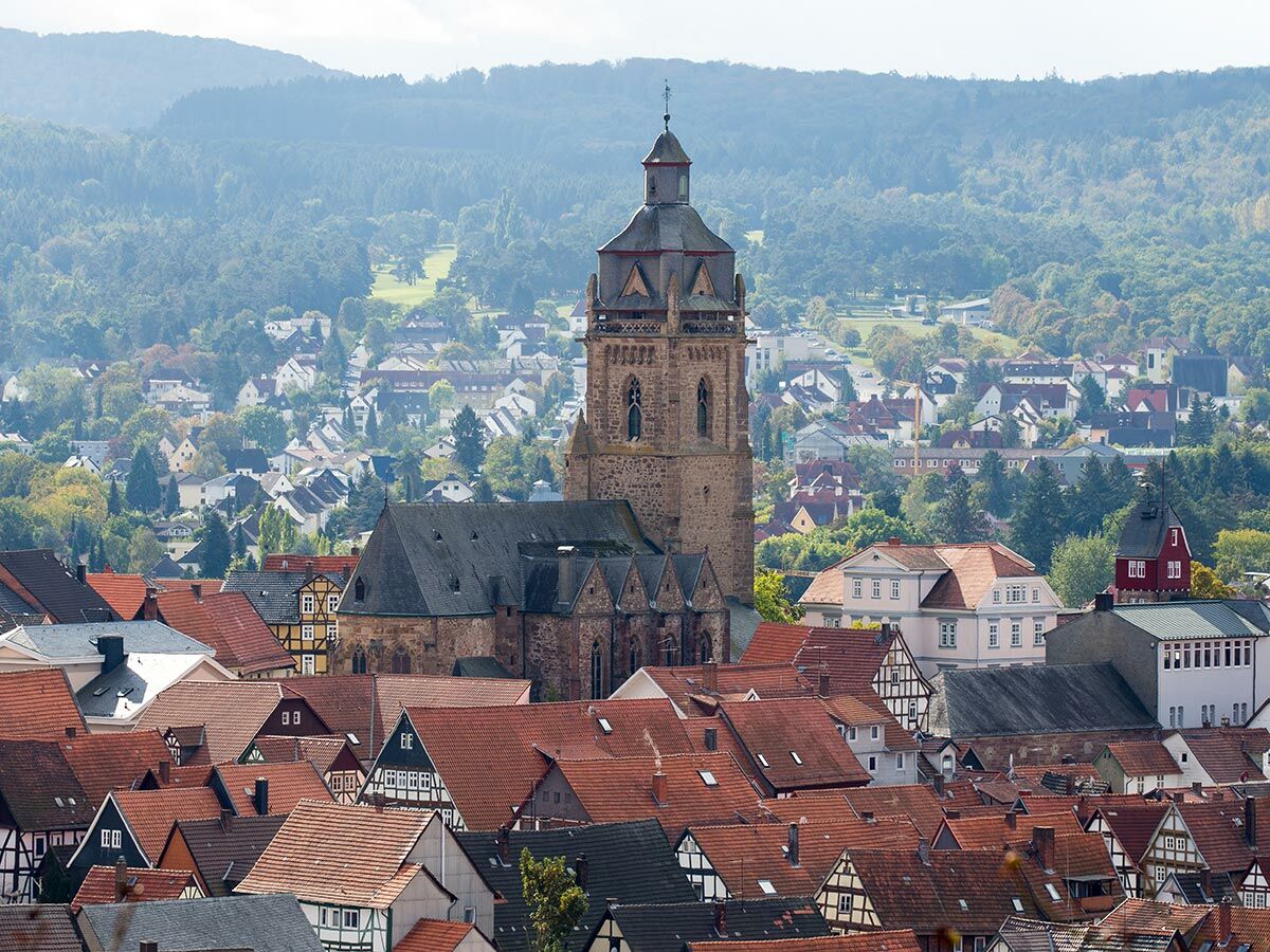 Panoramablick auf eine historische deutsche Stadt mit roten Ziegeldächern, einer großen Steinkirche und bewaldeten Hügeln.