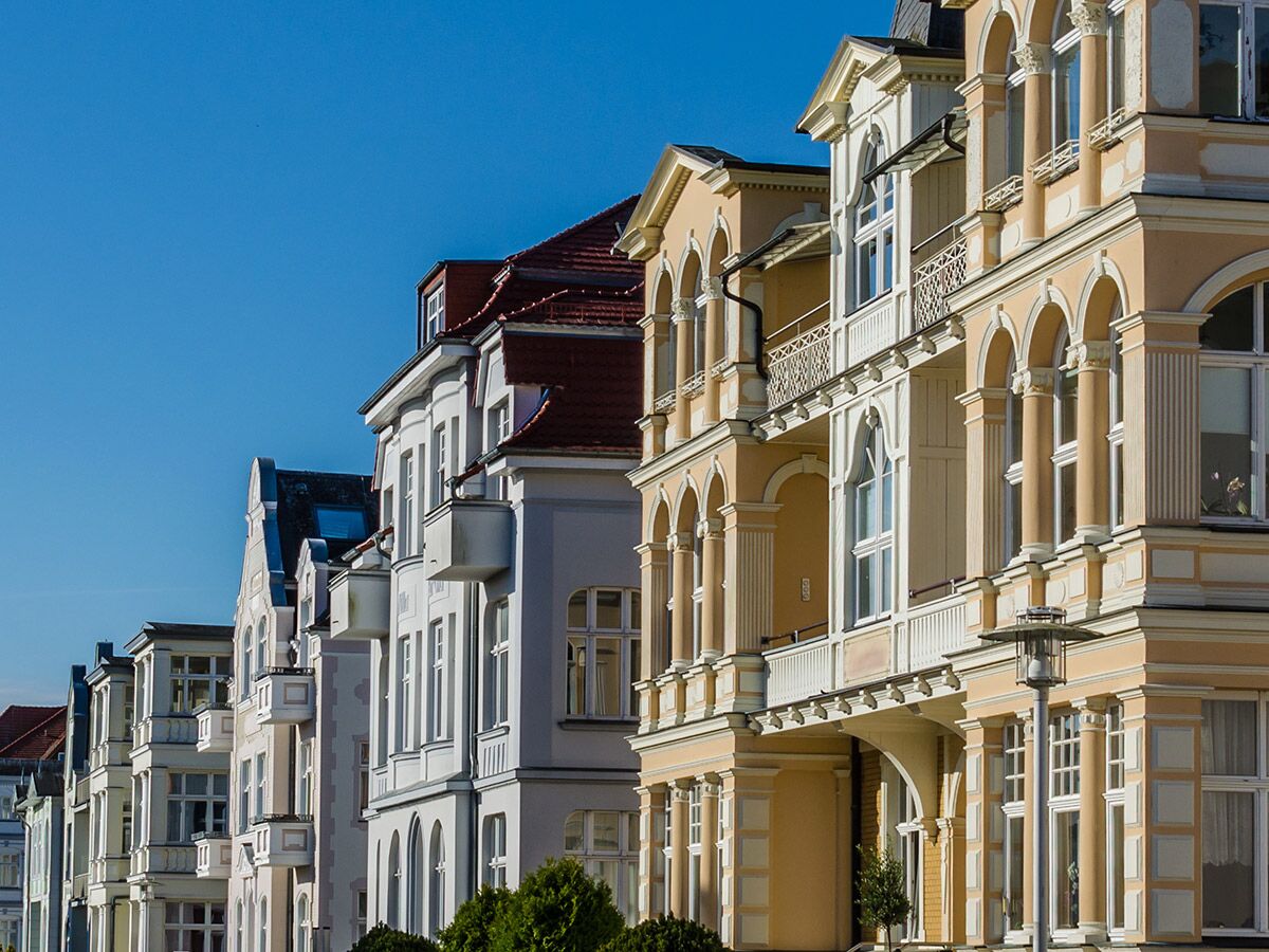 Reihe historischer Stadthäuser mit detailreichen Fassaden und Balkonen unter strahlend blauem Himmel an einem sonnigen Tag.