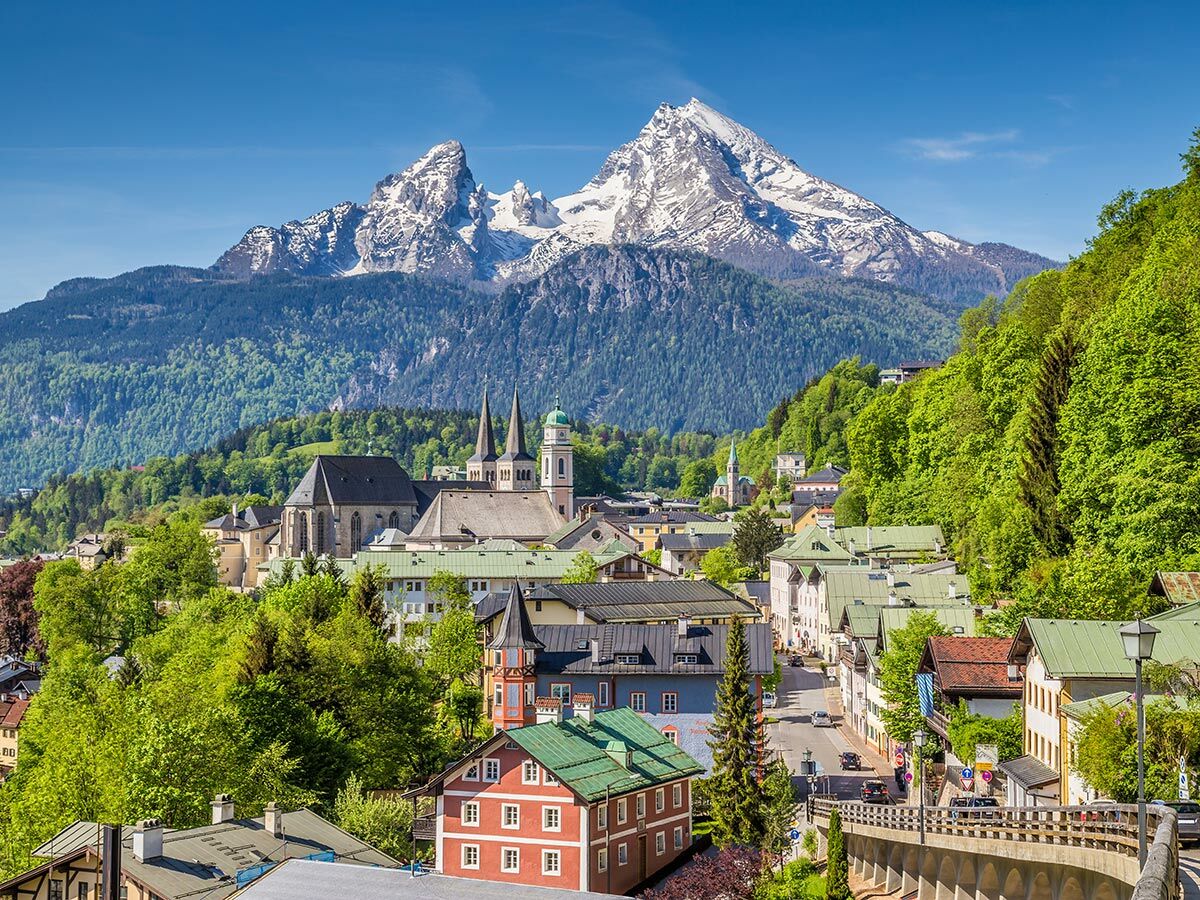 Panoramablick auf die bayerische Stadt Berchtesgaden mit historischen Gebäuden, Kirchen und dem majestätischen, schneebedeckten Watzmann im Hintergrund.