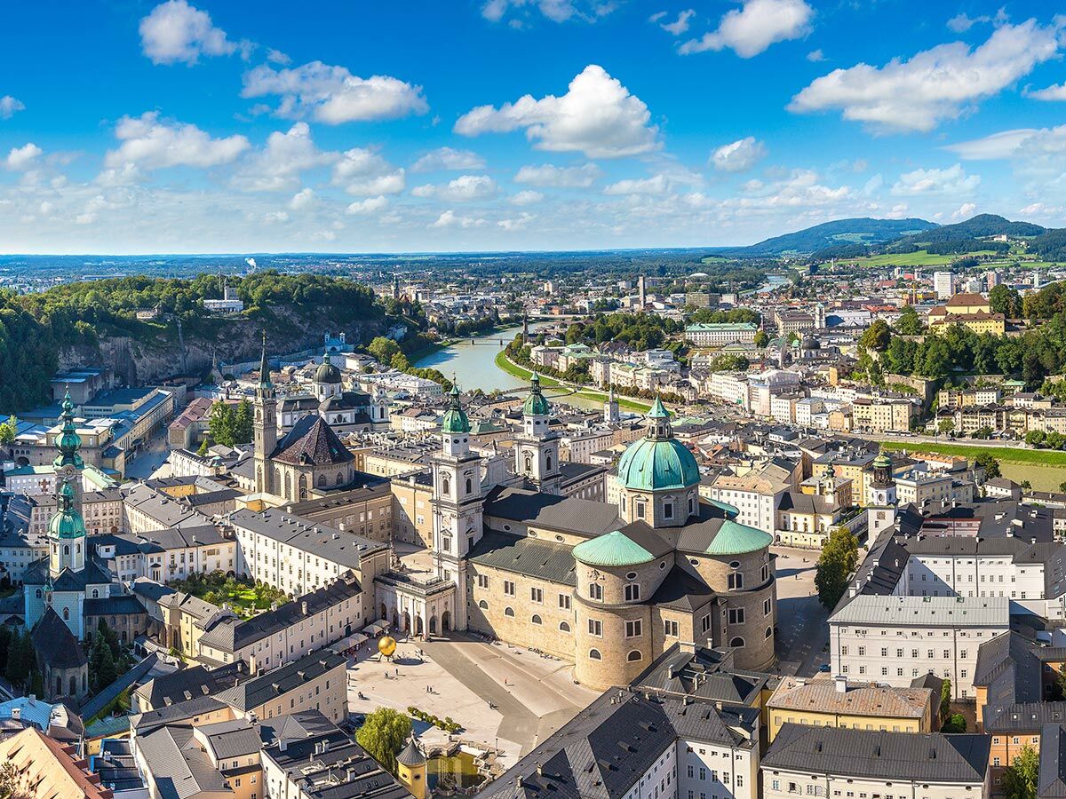 Luftbild von Salzburg, Österreich, mit der Salzburger Kathedrale, der Salzach und umgebenden Bergen unter blauem Himmel.