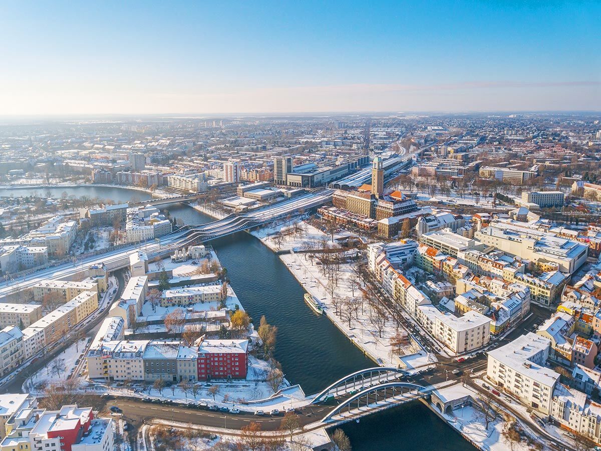 Winterliche Luftaufnahme von Leipzig mit Flüssen, verschneiten Dächern, Brücken und Hauptbahnhof unter blauem Himmel.
