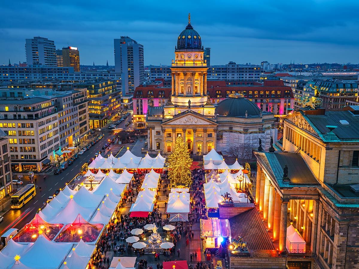 Beleuchteter Weihnachtsmarkt am Gendarmenmarkt in Berlin mit Dom und Konzerthaus bei Abenddämmerung.