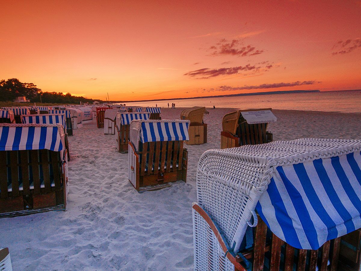 Zahlreiche blau-weiß gestreifte Strandkörbe am Binzer Sandstrand bei einem atemberaubenden Sonnenuntergang über der Ostsee.