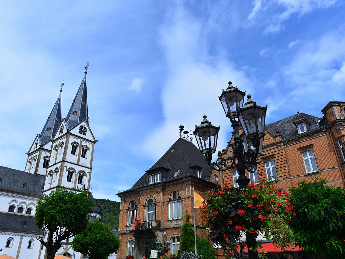 Historische Kirche mit zwei Türmen, traditionellen Gebäuden und Blumen an Straßenlaterne in europäischer Altstadt.