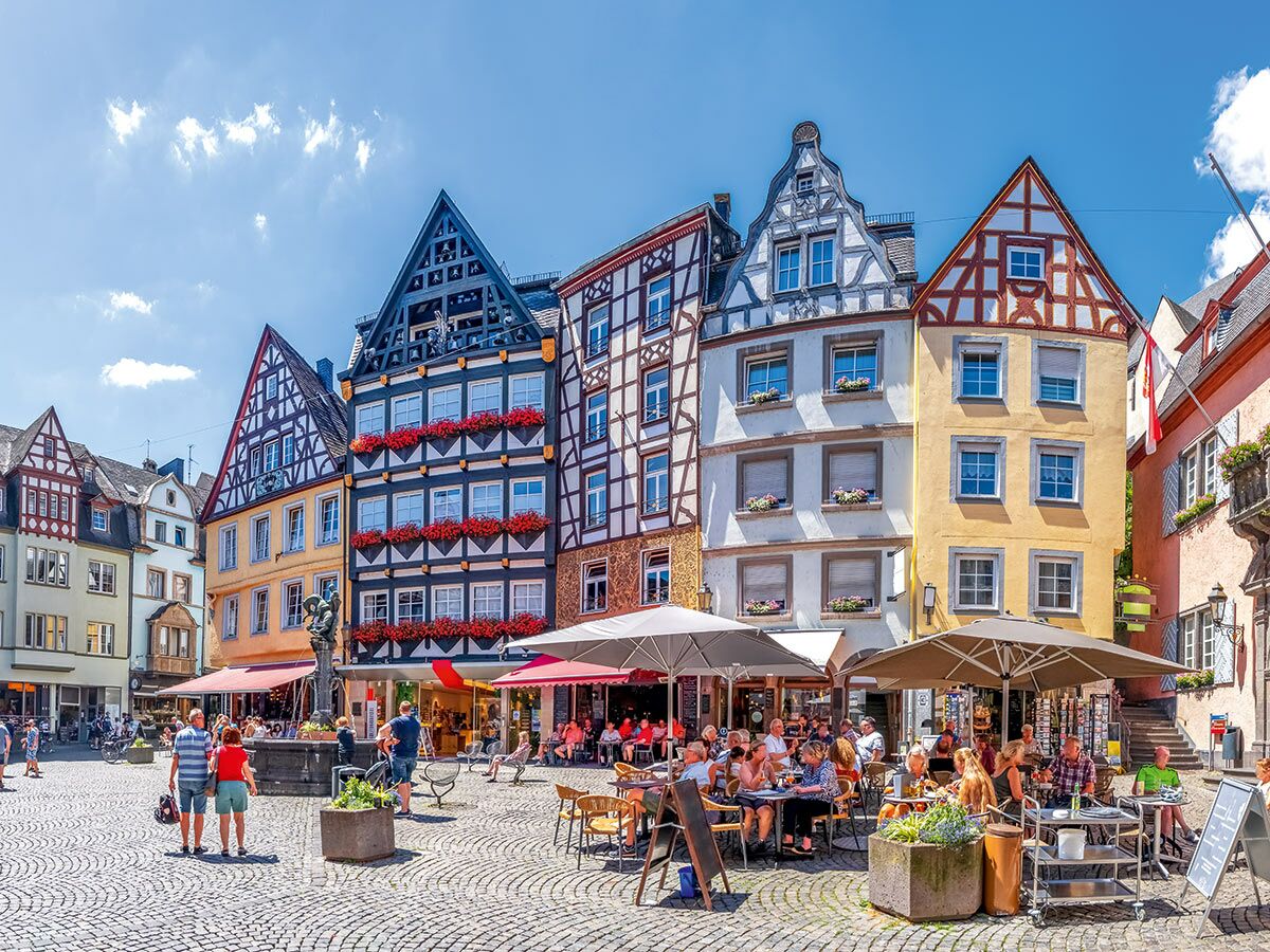 Belebter historischer Marktplatz mit farbenfrohen Fachwerkhäusern, Außenrestaurants und Menschen an einem sonnigen Sommertag in Deutschland.