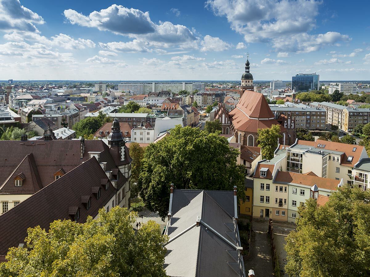 Luftaufnahme des Stadtzentrums von Luckau, Brandenburg, mit der markanten St. Nikolai Kirche, roten Dächern und grünen Bäumen unter blauem Himmel.