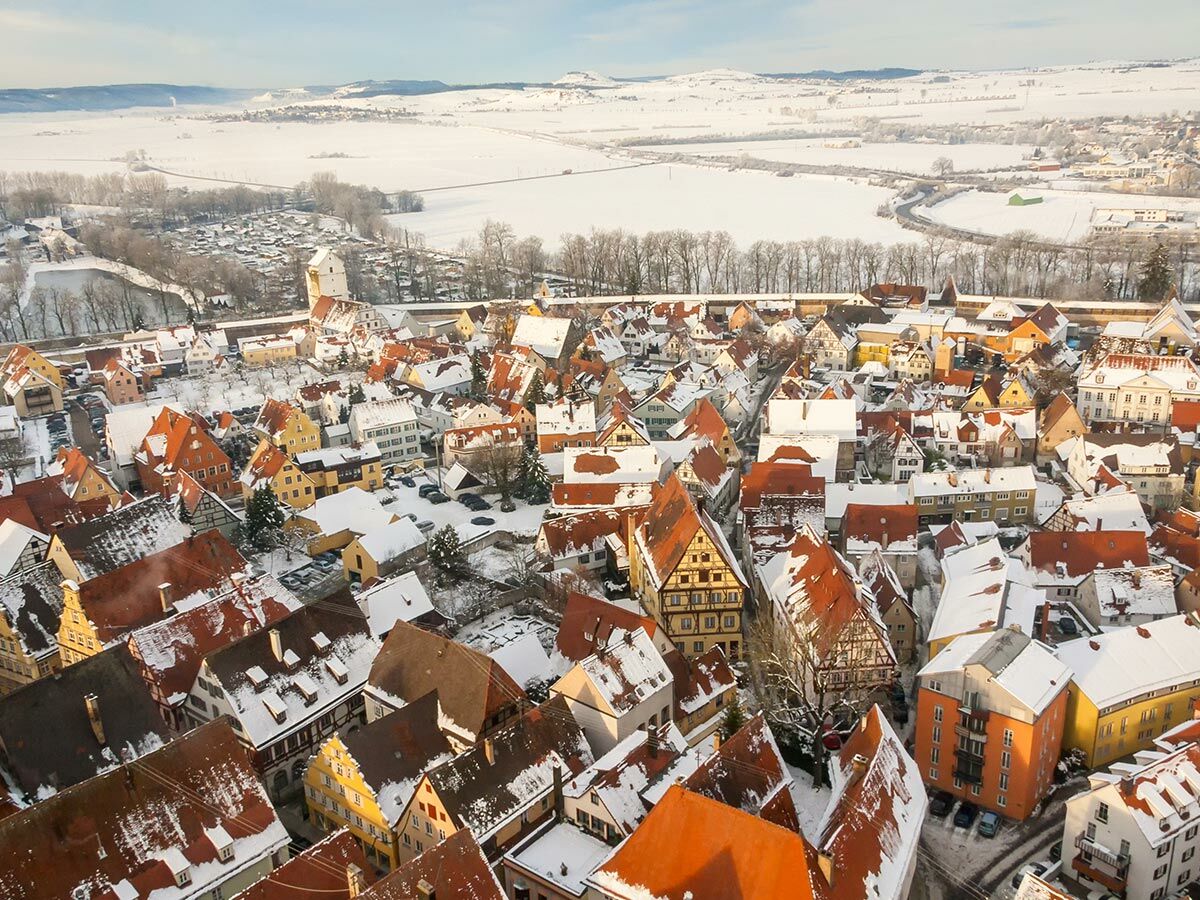 Luftbild einer verschneiten historischen Altstadt mit roten Ziegeldächern, umgeben von einer weiten, schneebedeckten Winterlandschaft.