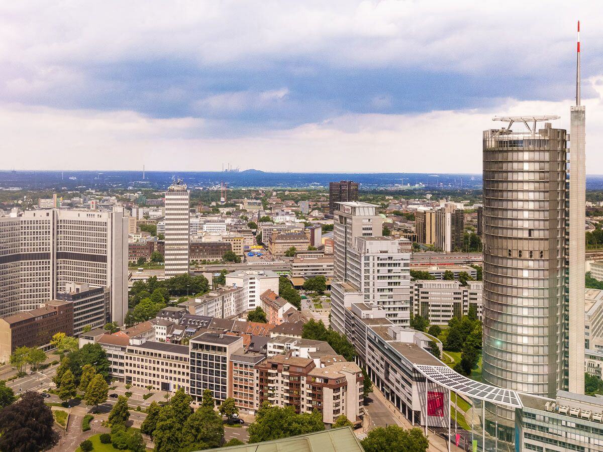 Luftaufnahme von Düsseldorf mit dem markanten Rheinturm, modernen Hochhäusern, grünen Parks und einer weiten Stadtlandschaft.