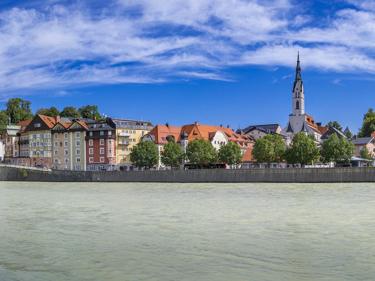 Historische Stadt Wasserburg am Inn mit bunten Häusern, St. Jakobskirche und Fluss Inn unter blauem Himmel.