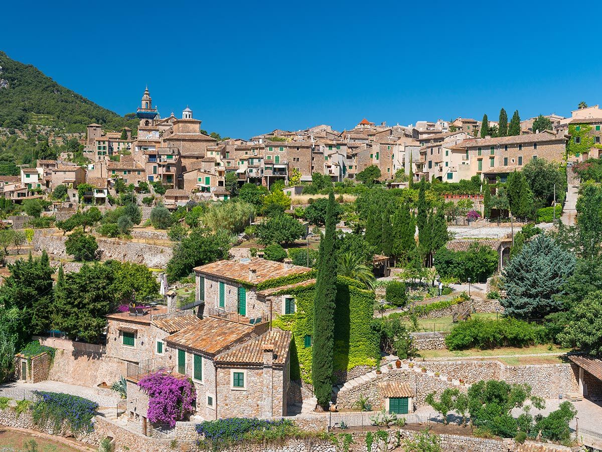 Malerisches Bergdorf Valldemossa, Mallorca: Steinhäuser, grüne Fensterläden, Kirche und üppige Gärten unter blauem Himmel.