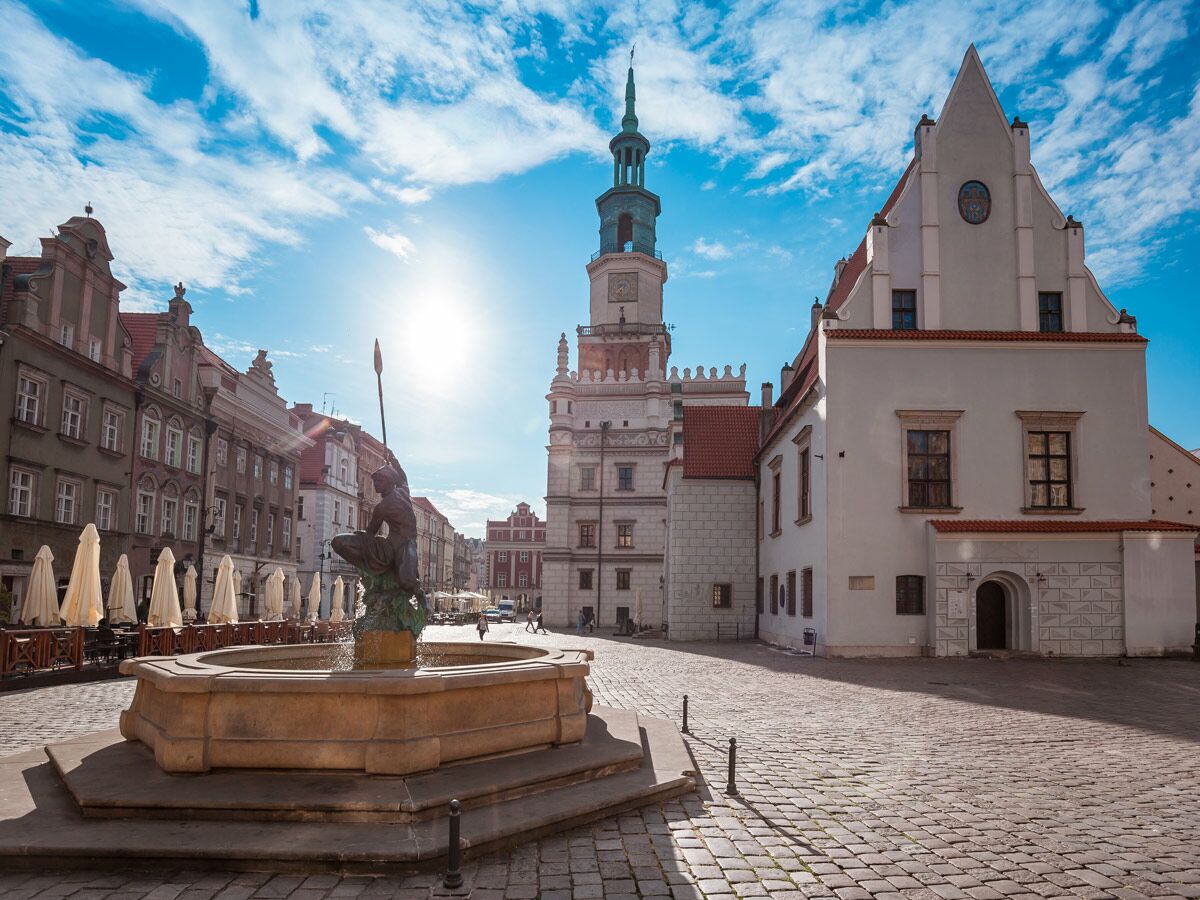 Sonniger Marktplatz in Poznań mit Neptunbrunnen, historischen Gebäuden und Rathausturm unter blauem Himmel.