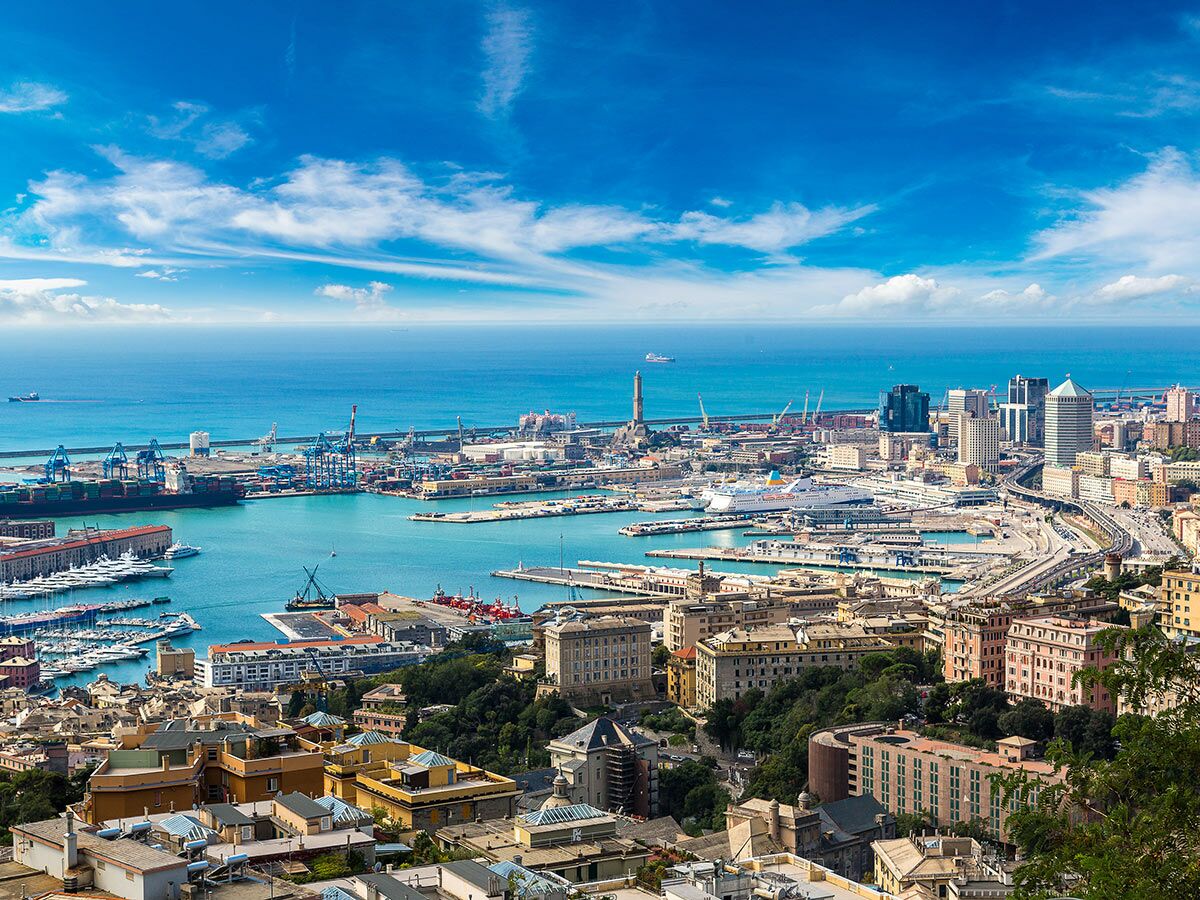 Panoramablick auf den geschäftigen Hafen von Genua mit Containerschiffen, Yachten, Kreuzfahrtschiffen, Stadtgebäuden und blauem Mittelmeer.