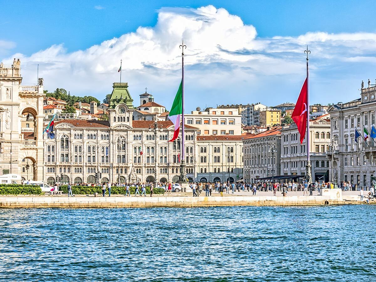 Triest, Italien: Piazza Unità d'Italia mit historischen Gebäuden, italienischer und türkischer Flagge, Menschen und Adria.