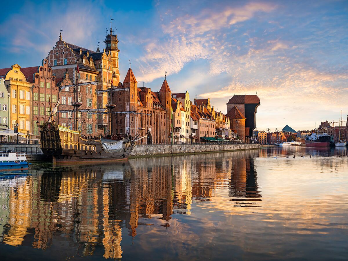 Malerische Danziger Altstadt Uferpromenade mit historischem Schiff, farbigen Gebäuden und dem Krantor, das sich im Fluss Motława spiegelt.