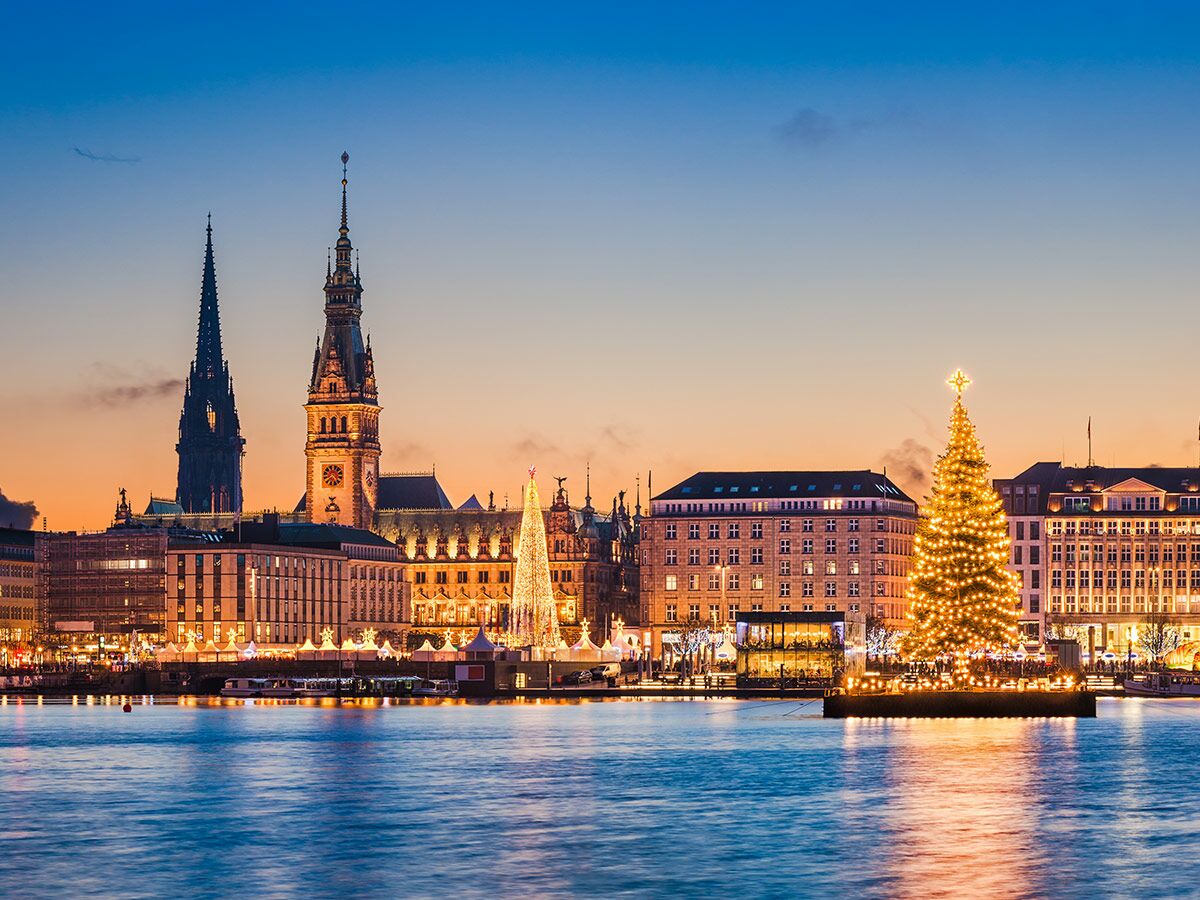Hamburg Skyline bei Sonnenuntergang mit beleuchtetem Rathaus, St. Nikolai und schwimmendem Weihnachtsbaum auf der Alster.
