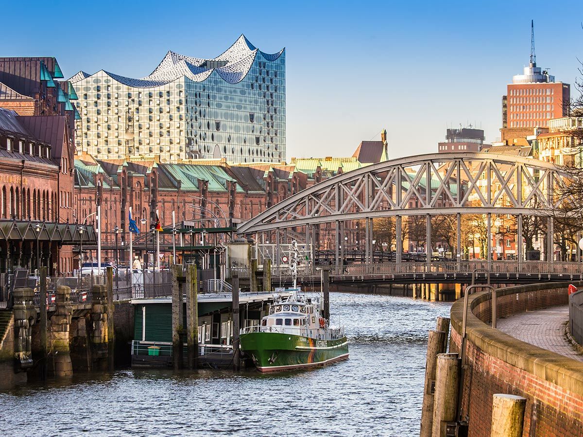 Panoramablick auf Hamburg mit Elbphilharmonie, Speicherstadt, Brücke und grünem Boot im sonnigen Kanal.