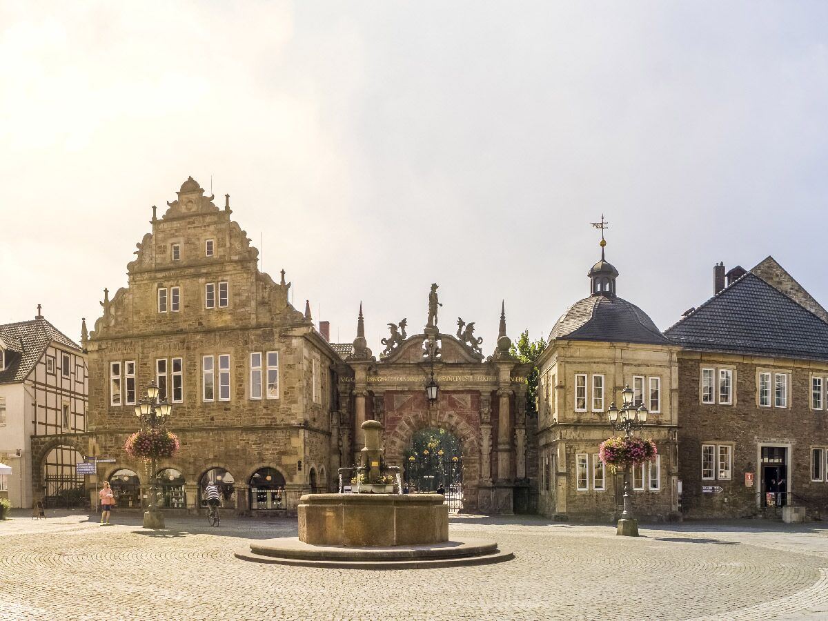 Blick auf einen historischen Marktplatz in Deutschland mit Sandsteingebäuden, einem Giebelhaus, Brunnen und einem verzierten Torbogen.