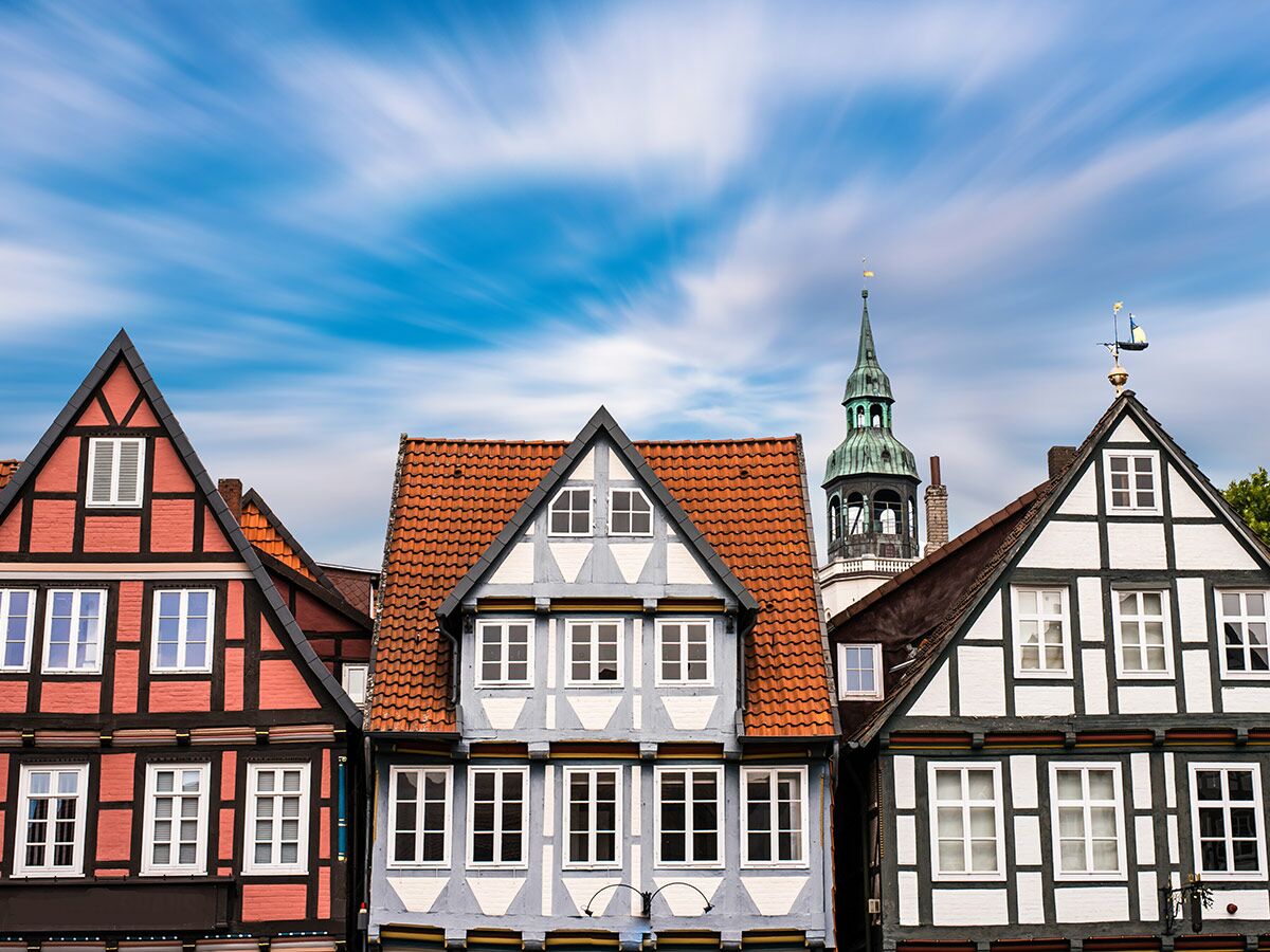 Reihe bunter Fachwerkhäuser mit traditioneller Architektur und Kirchturm unter langbelichtetem Himmel in einer Altstadt.