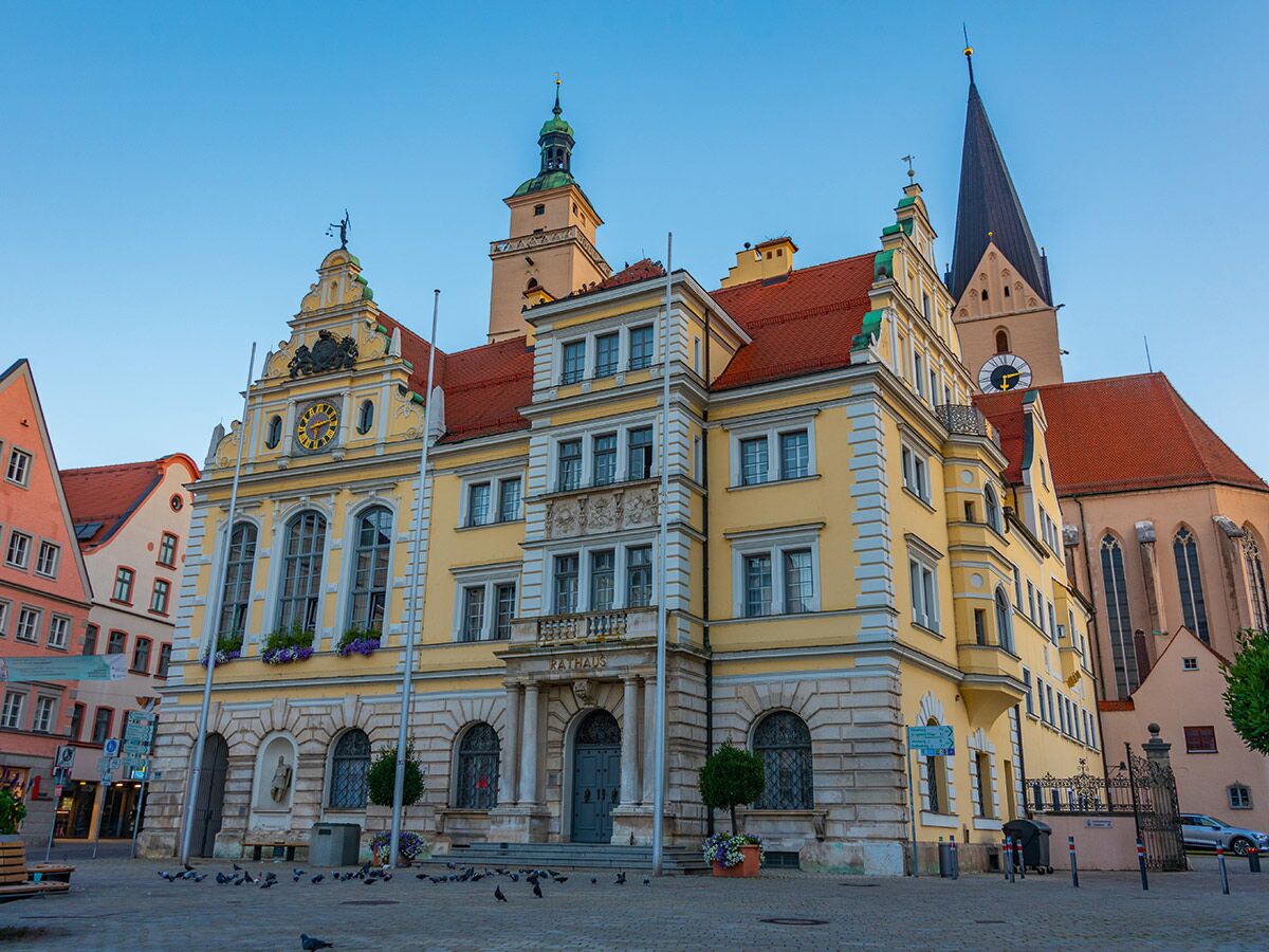 Historisches gelbes Rathaus in Landsberg am Lech mit Uhr und Turm, umgeben von weiteren Gebäuden und Kirche.