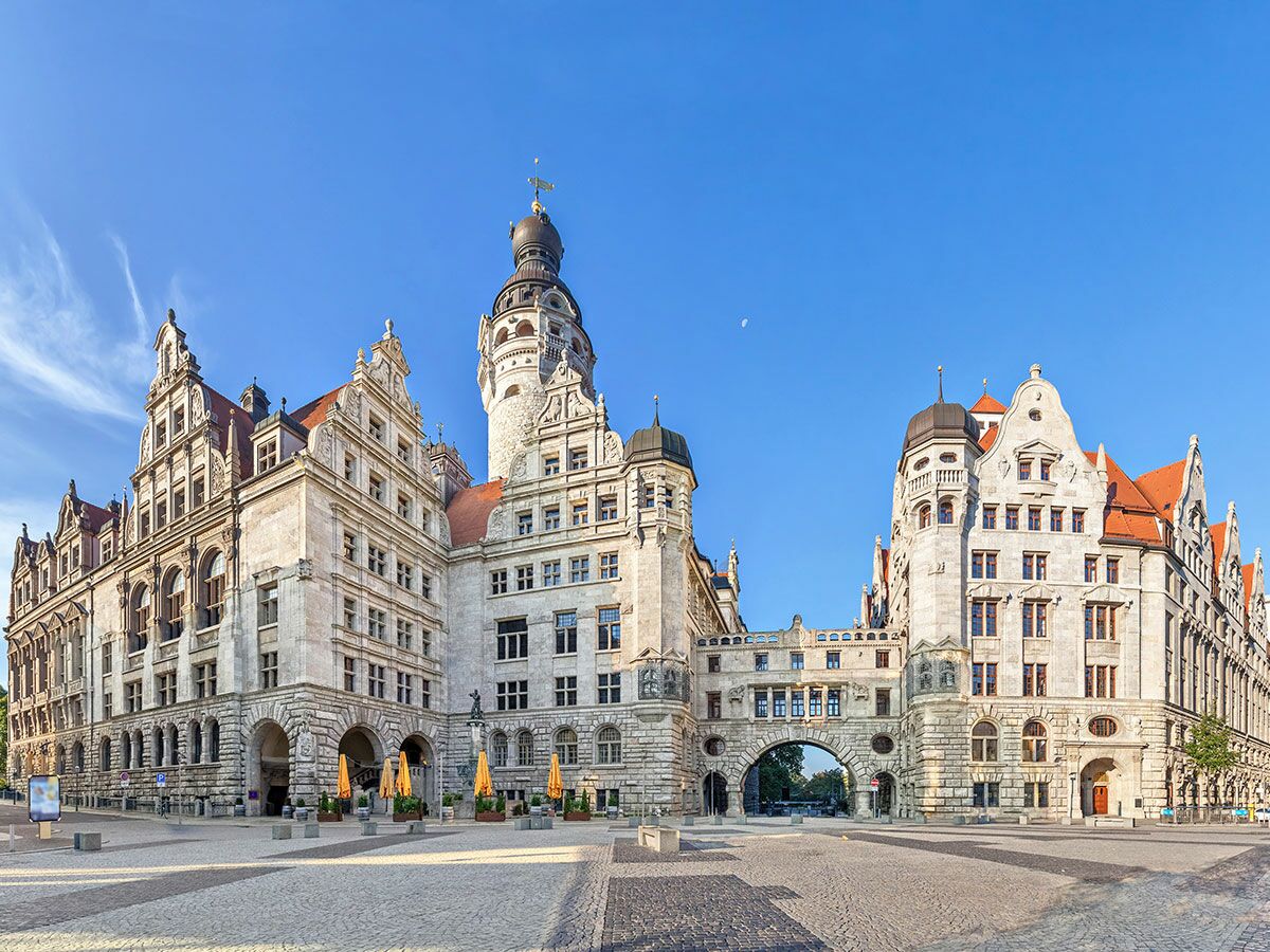 Neues Rathaus Leipzig, Deutschland, mit markantem Turm, Giebeln und Durchgangsbogen unter blauem Himmel und Sonnenlicht.