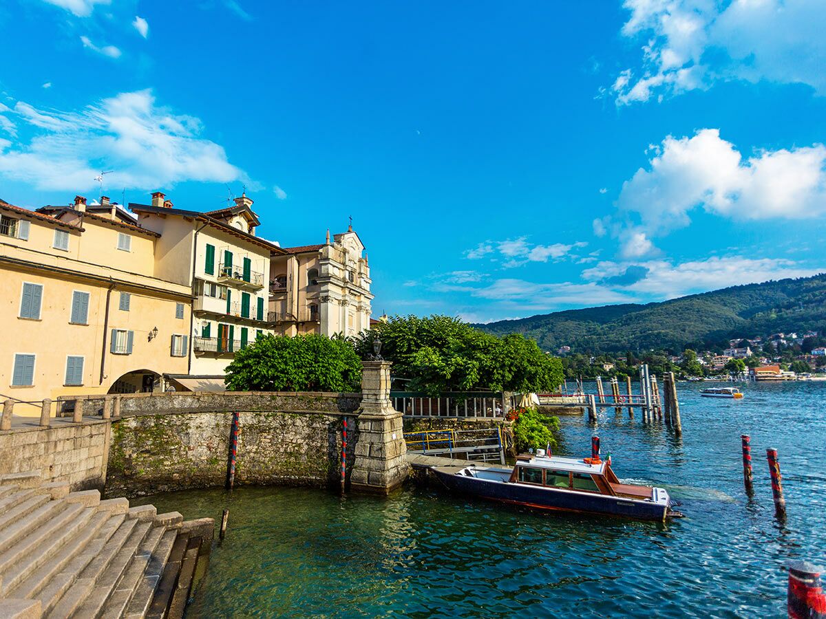 Malerische Ansicht von Orta San Giulio am Ortasee in Italien mit bunten Häusern, Kirche und Booten am Kai unter blauem Himmel.