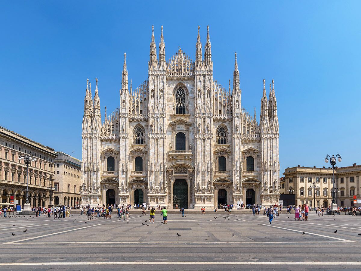 Die prächtige Fassade des Mailänder Doms (Duomo di Milano) an einem sonnigen Tag auf dem belebten Platz mit Touristen.