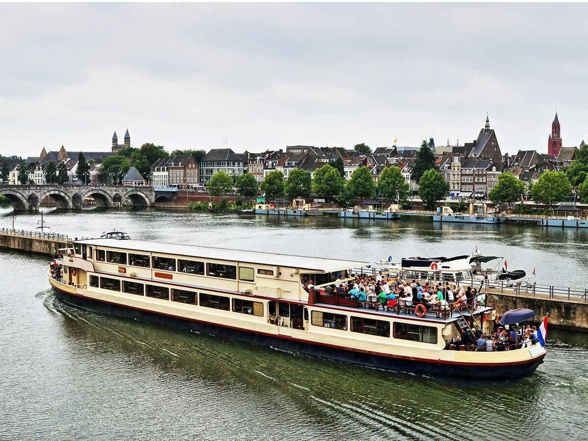 Passagierboot mit Touristen auf der Maas in Maastricht, Niederlande, vor historischer Stadtkulisse und St. Servaasbrug.
