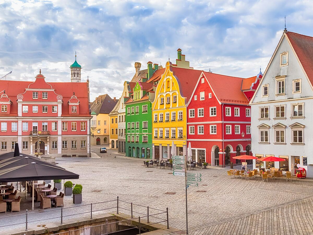 Bunter Stadtplatz in Landsberg am Lech mit historischen Gebäuden, Außengastronomie und gepflastertem Marktplatz unter blauem Himmel.