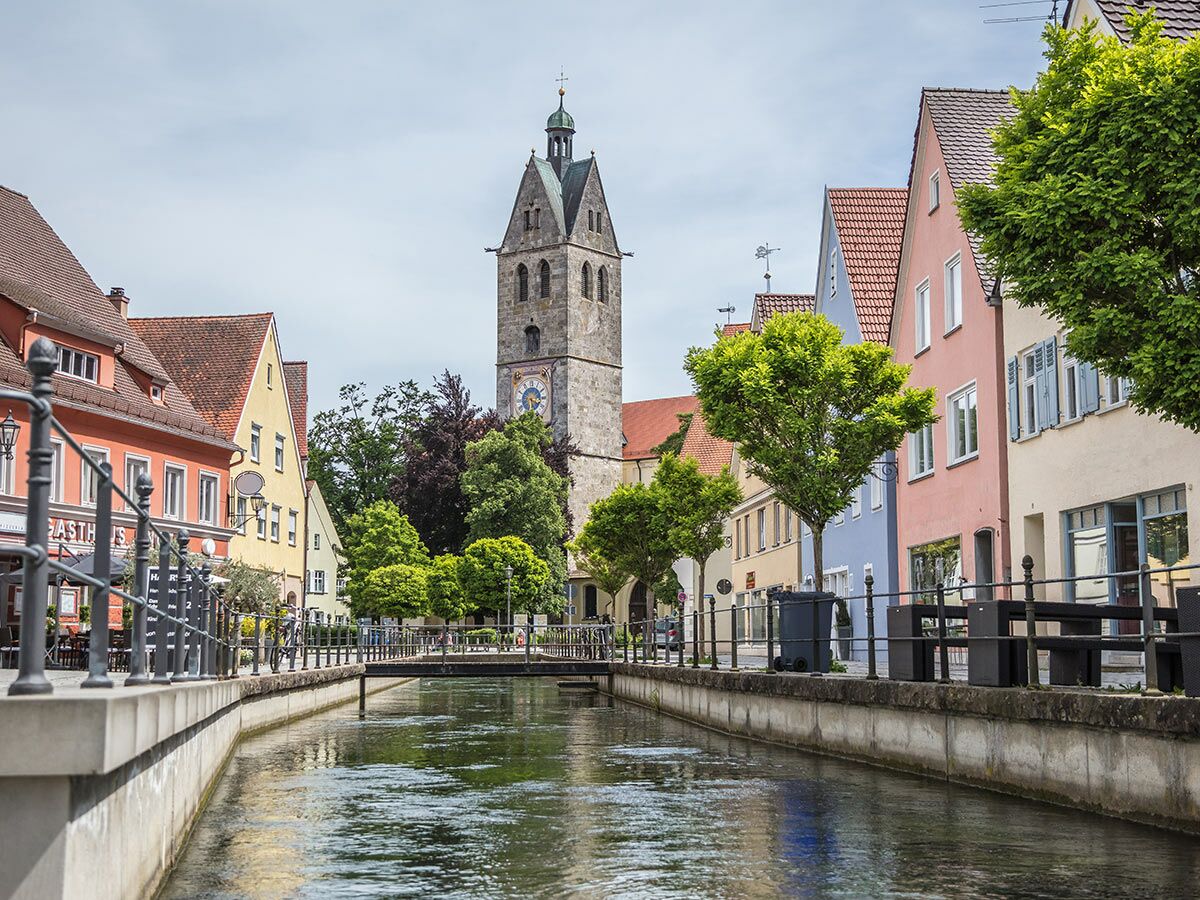 Historische europäische Stadt mit Kanal, bunten Häusern und markanter Kirche unter bewölktem Himmel. Idyllische Ansicht.