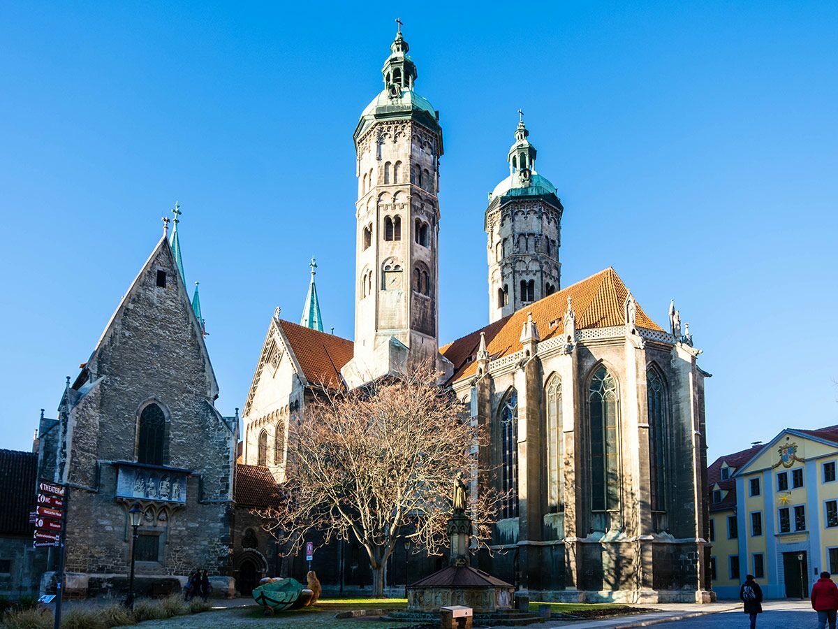Naumburger Dom St. Peter und Paul mit imposanten Türmen unter blauem Himmel und einem kahlen Baum im Vordergrund.