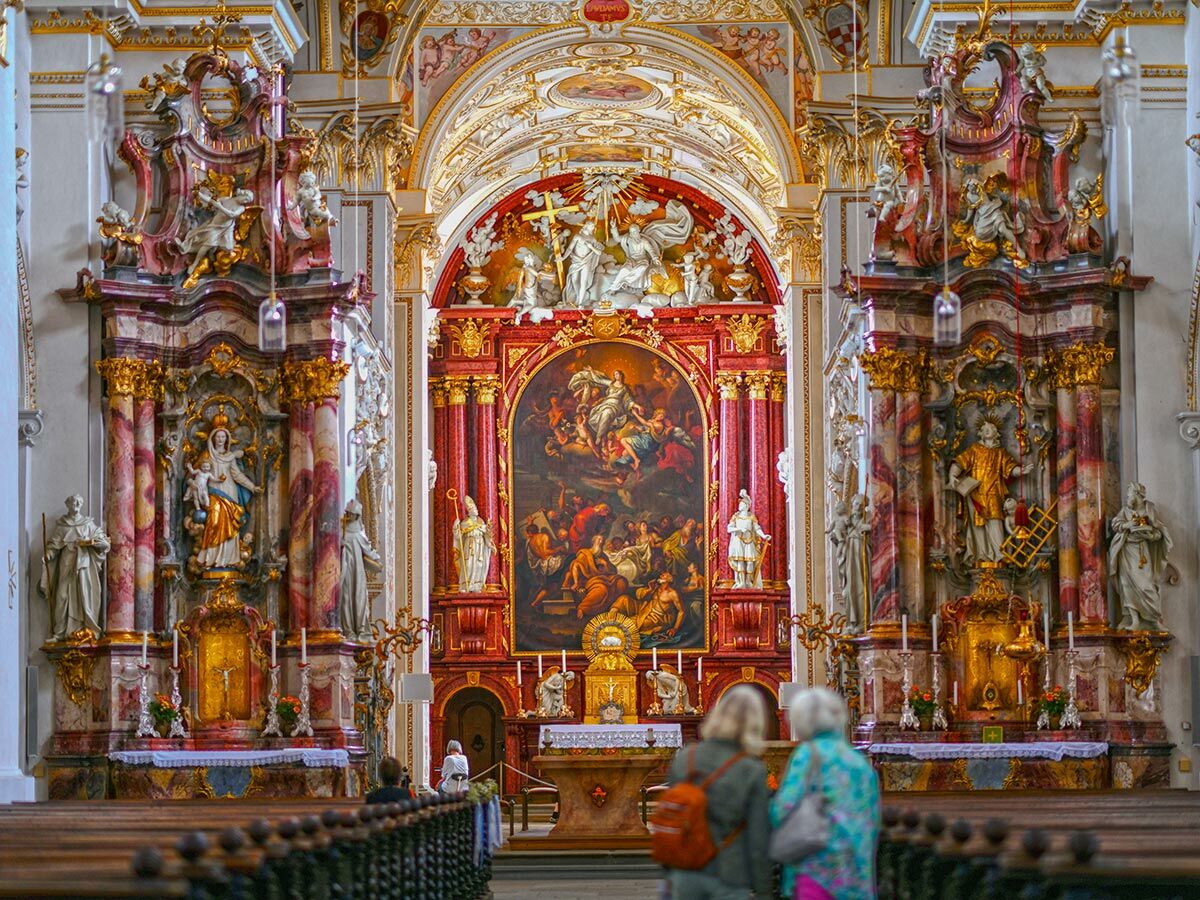 Blick in eine prunkvolle barocke Kirche mit aufwendig verziertem Hochaltar, großer Altartafel, Marmorsäulen und Heiligenfiguren.
