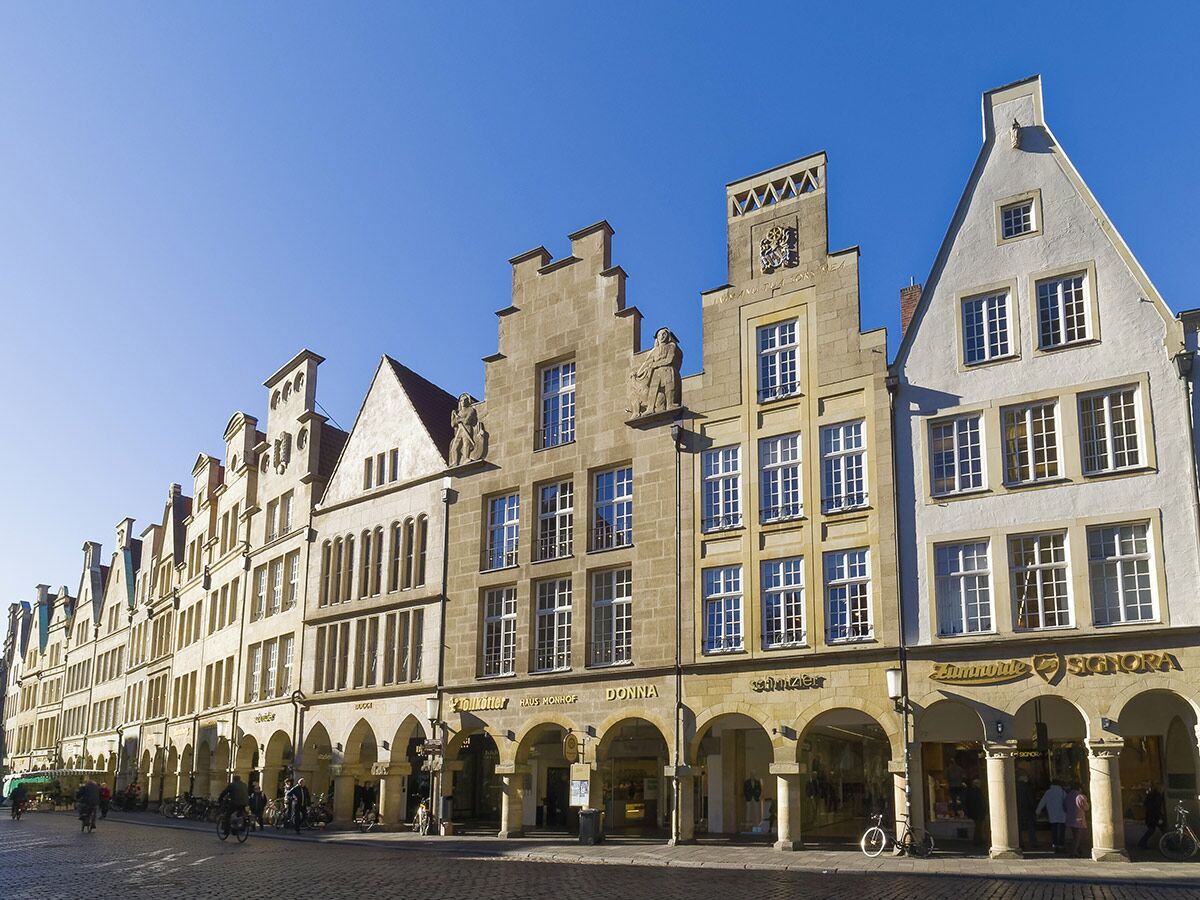 Blick auf den Prinzipalmarkt in Münster mit historischen Giebelhäusern, Arkaden und Geschäften unter blauem Himmel.