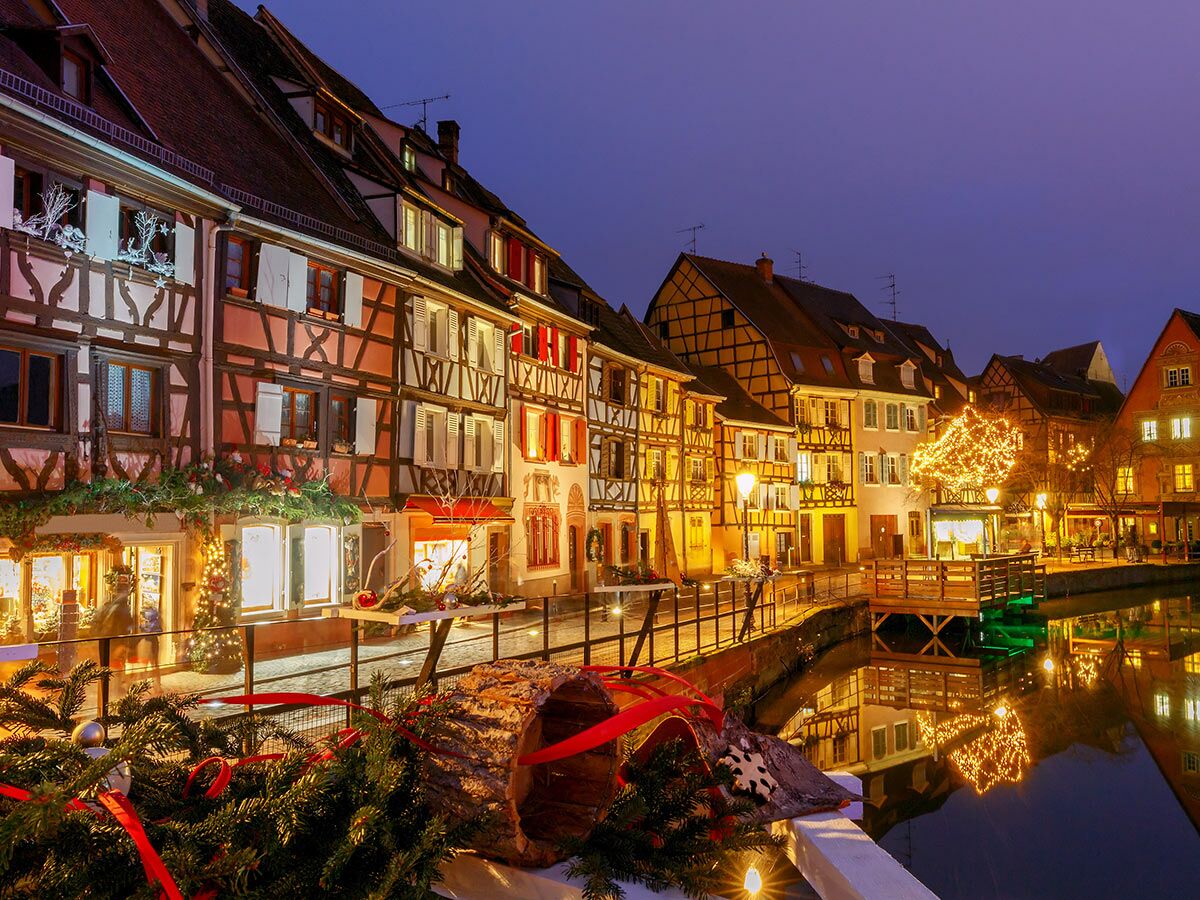 Romantische Fachwerkhäuser in Colmar, Frankreich, festlich mit Weihnachtslichtern geschmückt, spiegeln sich im ruhigen Kanal.
