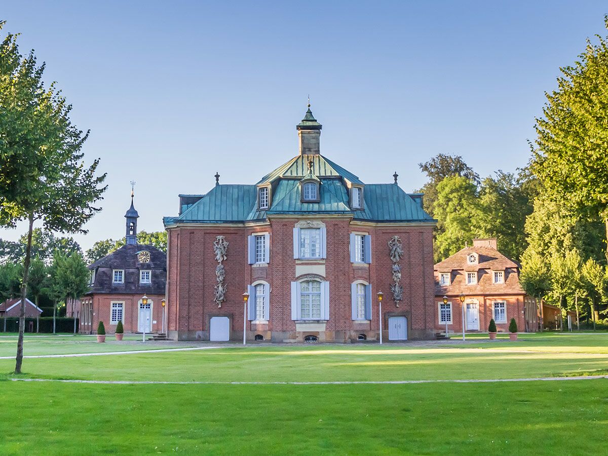 Barockschloss Nordkirchen mit roter Backsteinfassade und grünem Kupferdach, umgeben von einem grünen Park unter blauem Himmel.