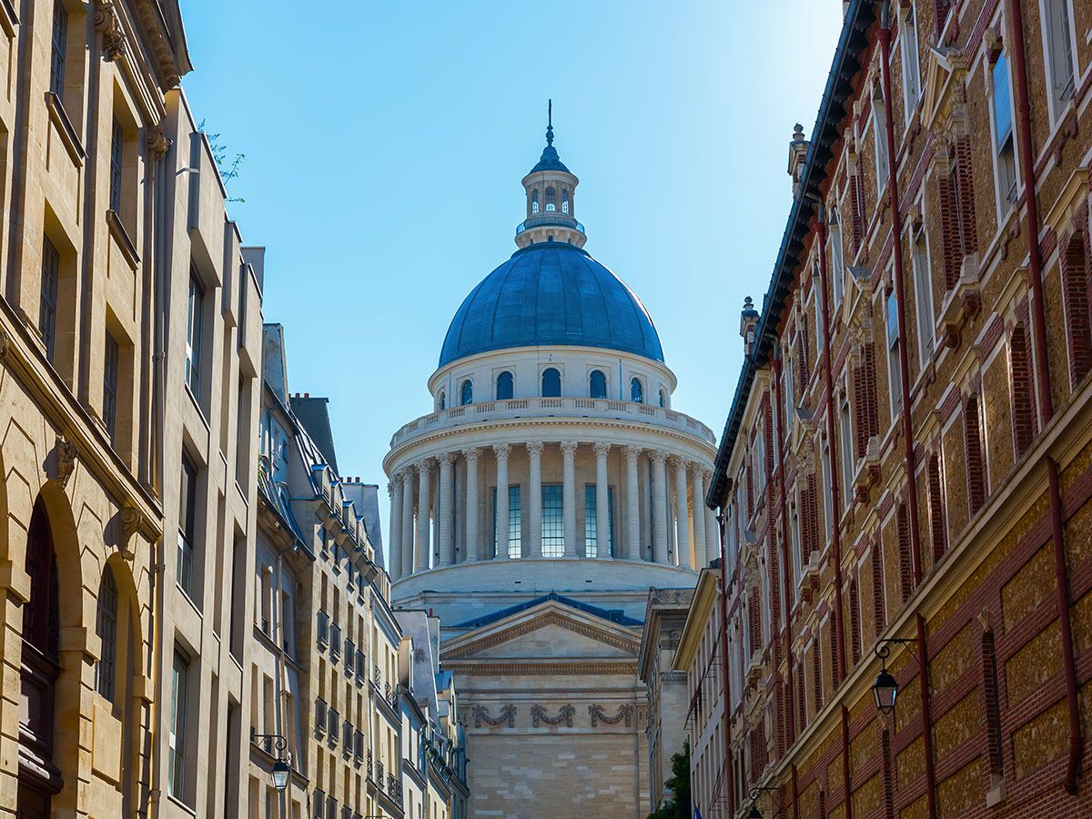 Das Pariser Pantheon, ein imposantes Denkmal mit Kuppel und Säulen, umrahmt von historischen Gebäuden an einem sonnigen Tag.