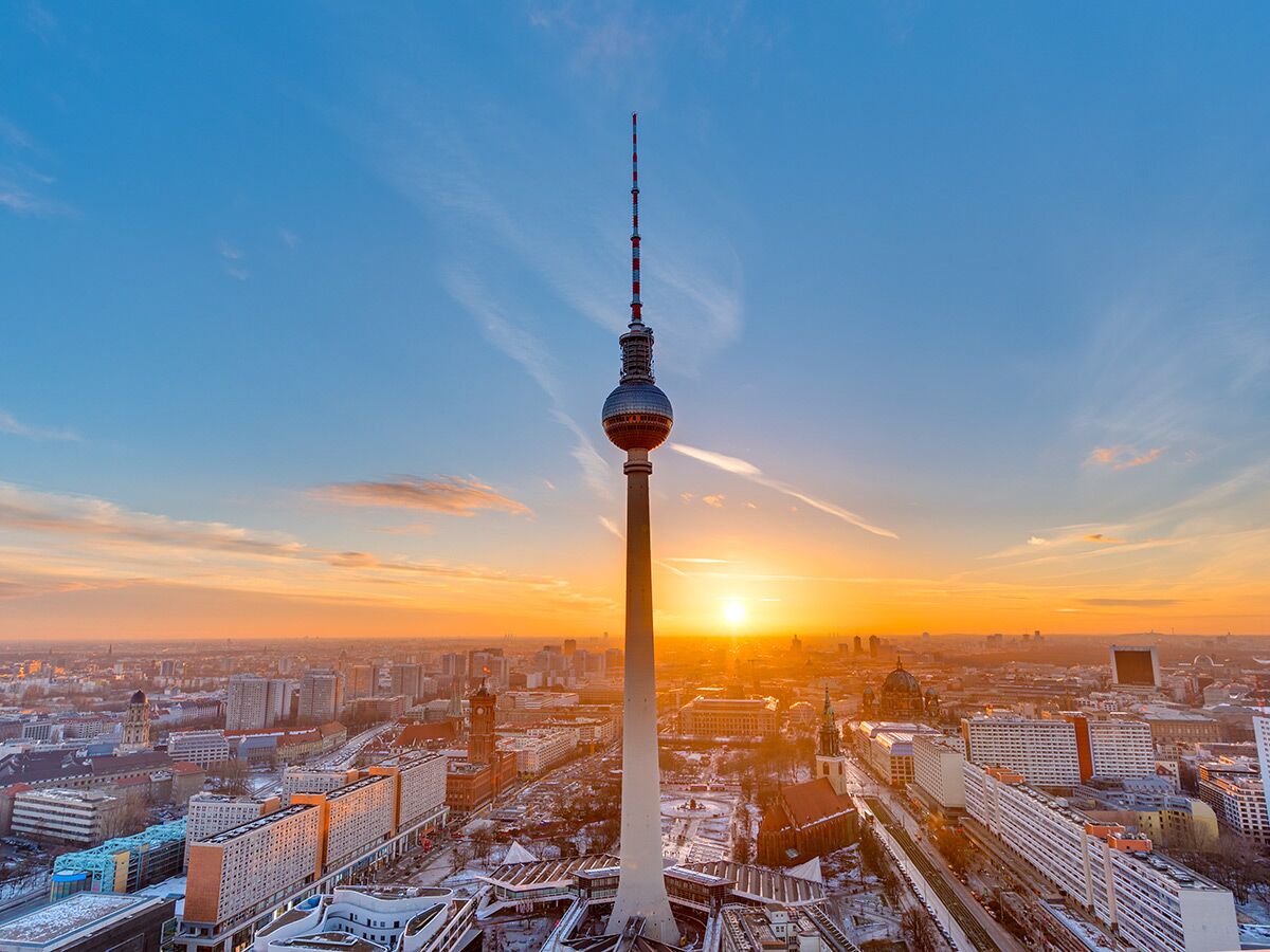 Der Berliner Fernsehturm ragt markant über die Dächer der Stadt Berlin bei Sonnenuntergang mit warmem Licht.