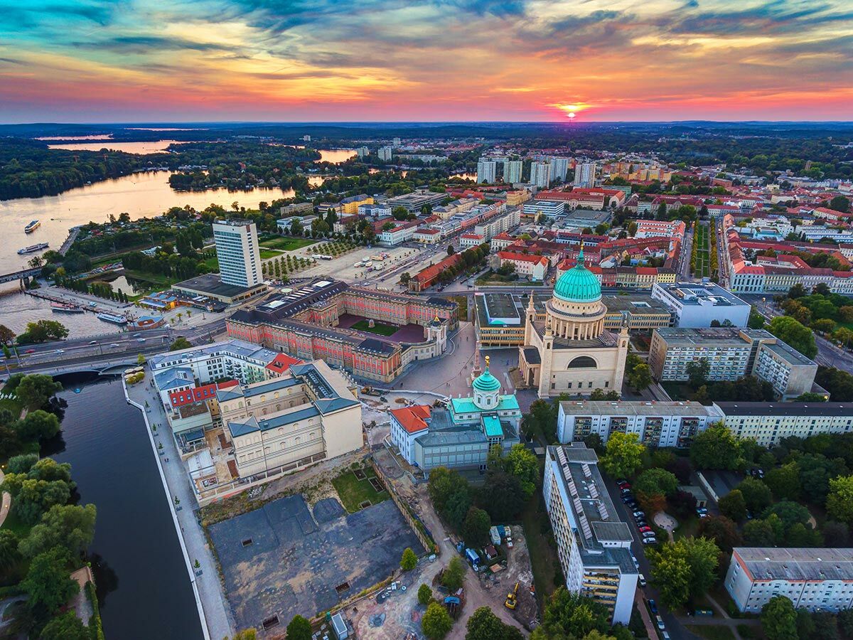 Luftaufnahme von Potsdam bei Sonnenuntergang, zeigt die St. Nikolaikirche, das Stadtschloss und die Havel mit Booten.