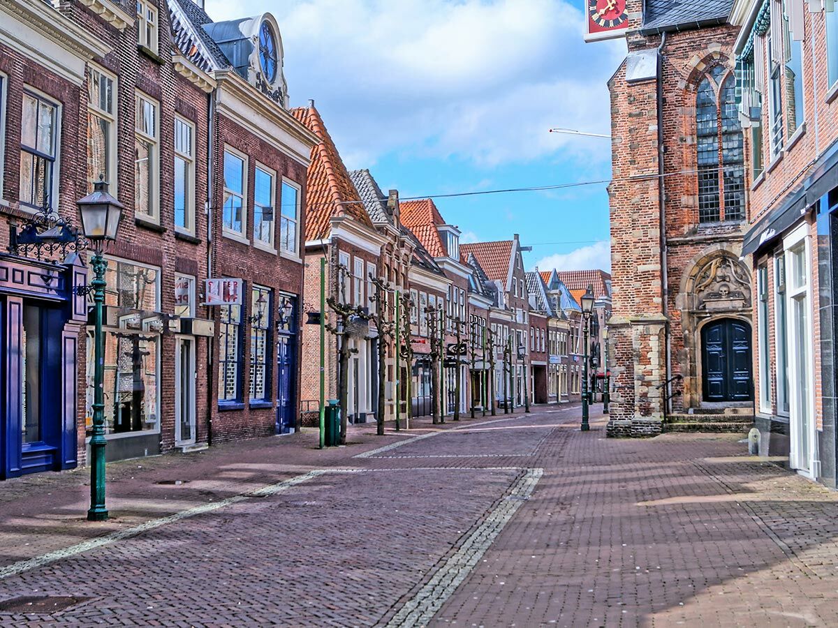 Blick auf eine historische holländische Gasse mit Kopfsteinpflaster, gesäumt von Backsteinhäusern und einer Kirche unter blauem Himmel.