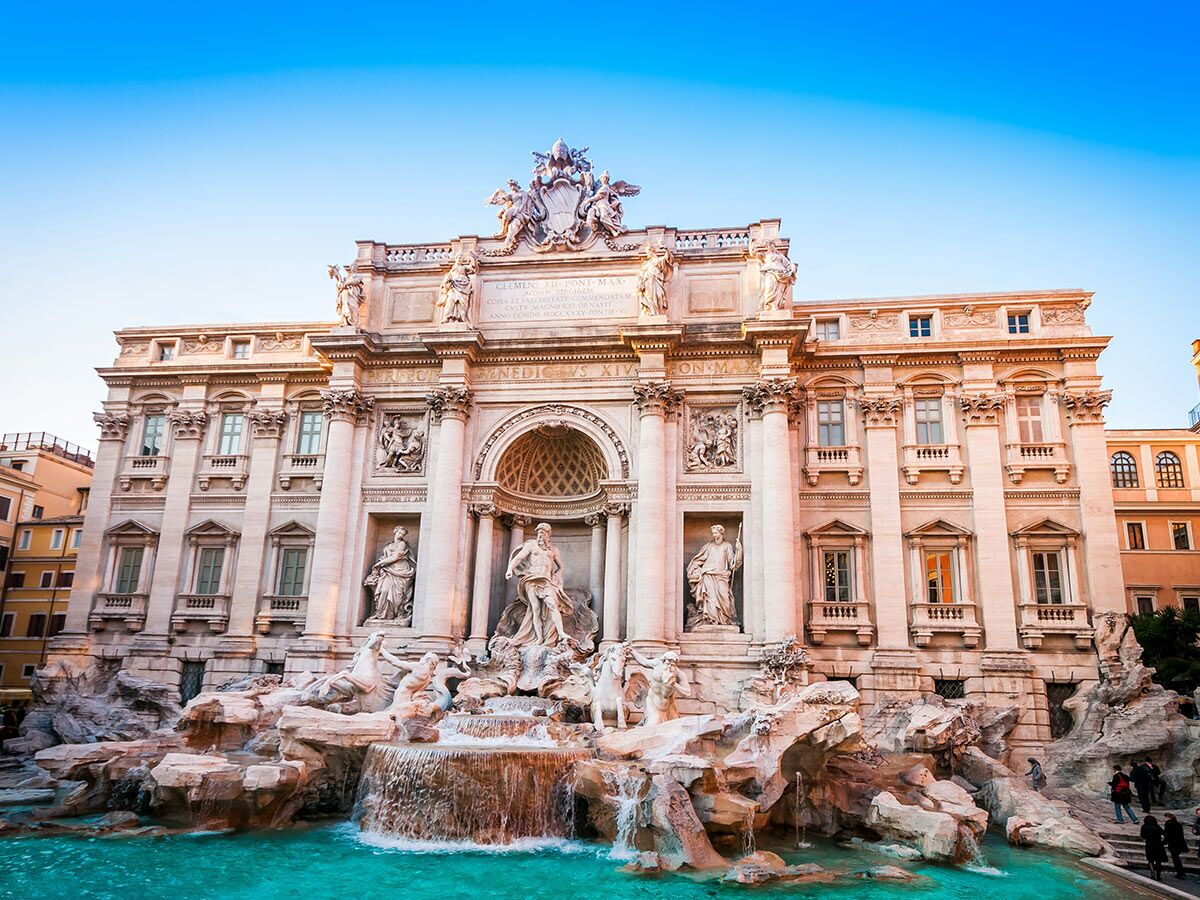 Der majestätische Trevi Brunnen in Rom bei Tageslicht mit blauer Himmel, zeigt Barockskulpturen und türkisblaues Wasser.